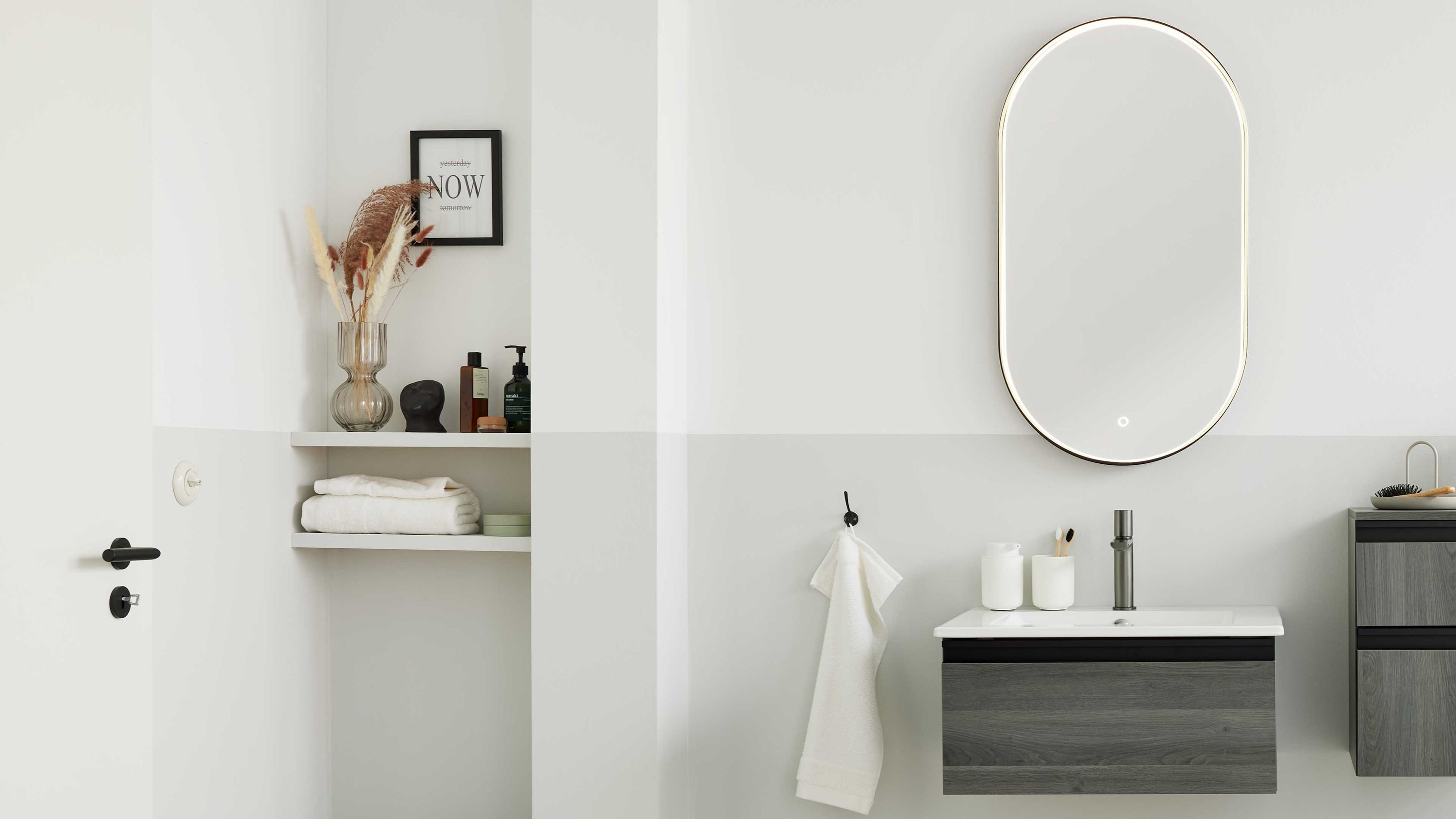 Dreiteiliges Badmöbel-Set mit grauen Fronten und weißem Waschbecken unter ovalem Spiegel an weißer Wand