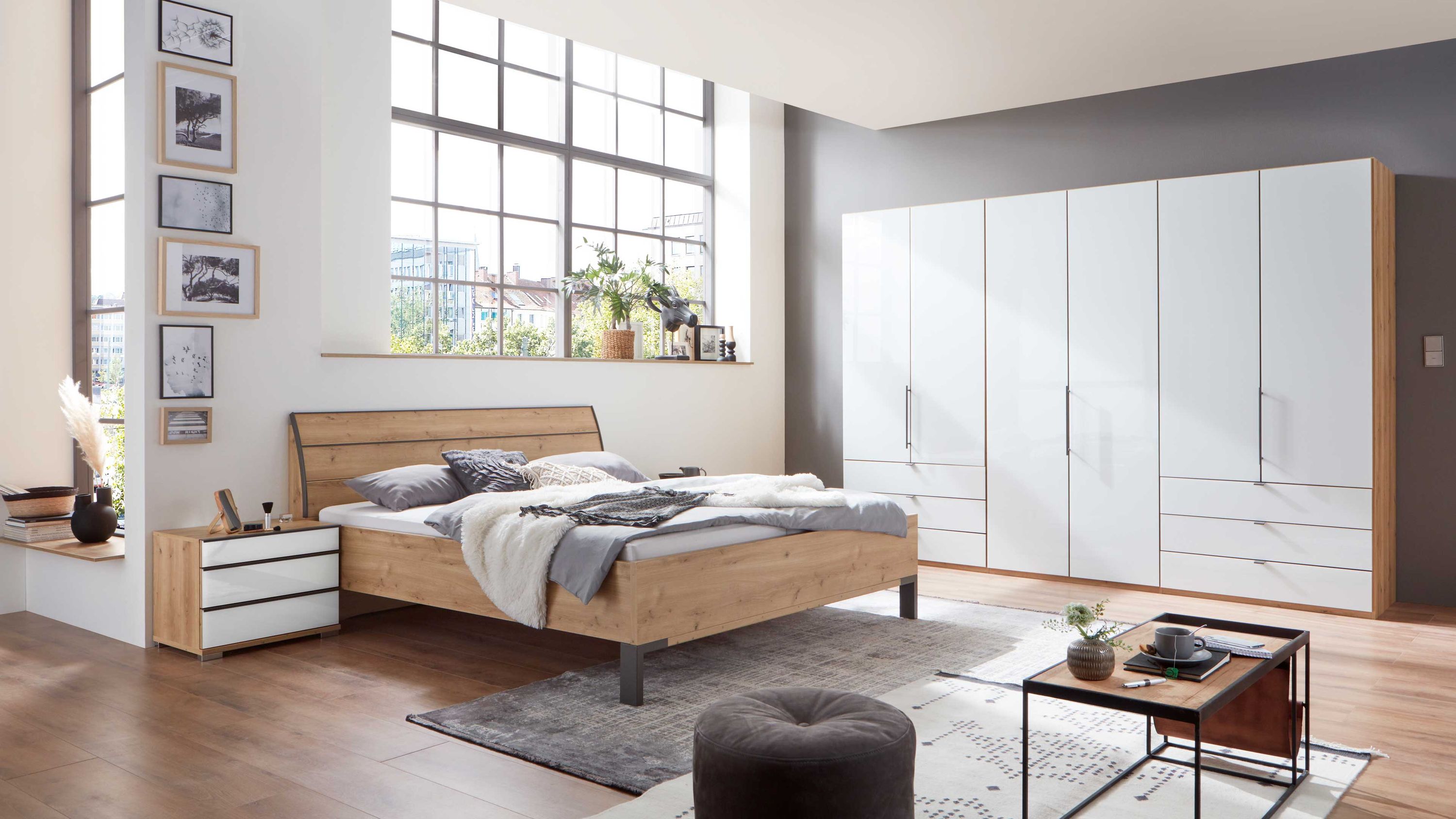 Schlafzimmer mit Bett Nachttisch und großem Kleiderschrank in Holzoptik und weißen Fronten