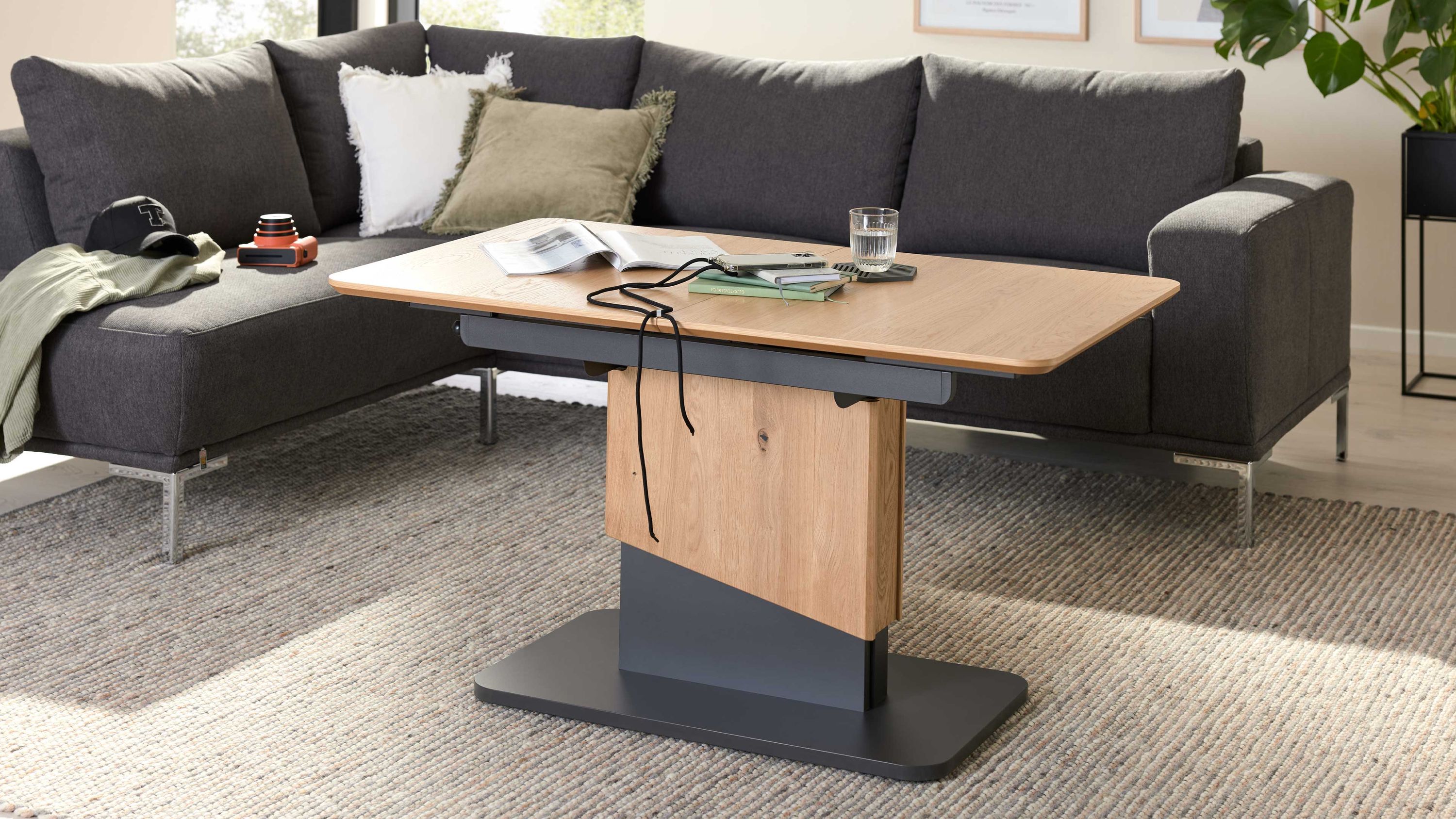 Couchtisch mit Holzplatte und schwarzem Sockel vor Sofa Rechteckiger Couchtisch mit Holzplatte und schwarzem Sockel vor grauem Ecksofa auf Teppich