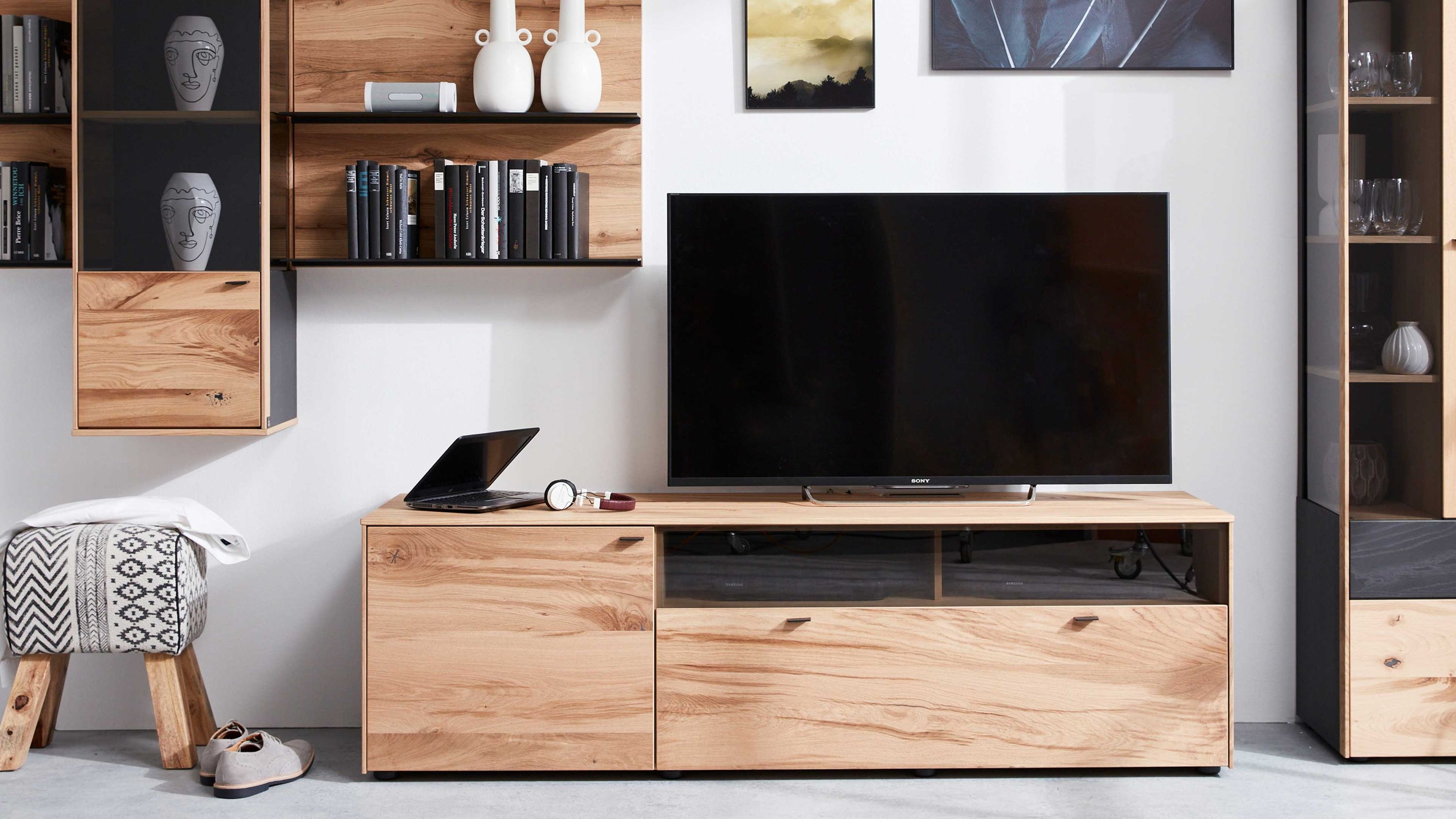Lowboard in Holzoptik mit anthrazitfarbenen Griffen und Fernseher Lowboard mit zwei Türen und zwei offenen Fächern in Holzoptik und anthrazitfarbenen Griffen mit Fernseher darauf