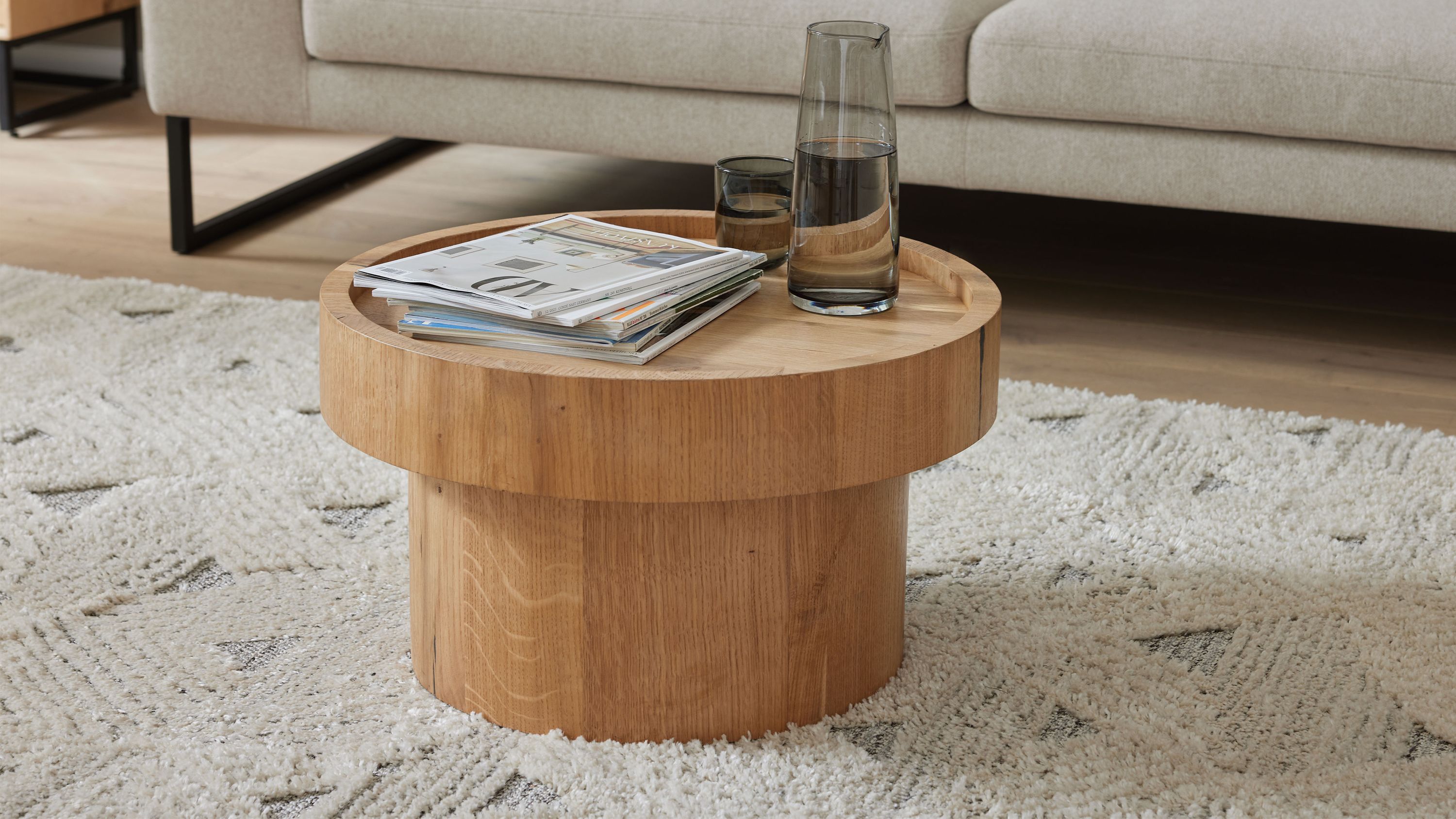 Runder Couchtisch mit Holzfurnier in natürlicher Farbe auf hellem Teppich vor beigem Sofa
