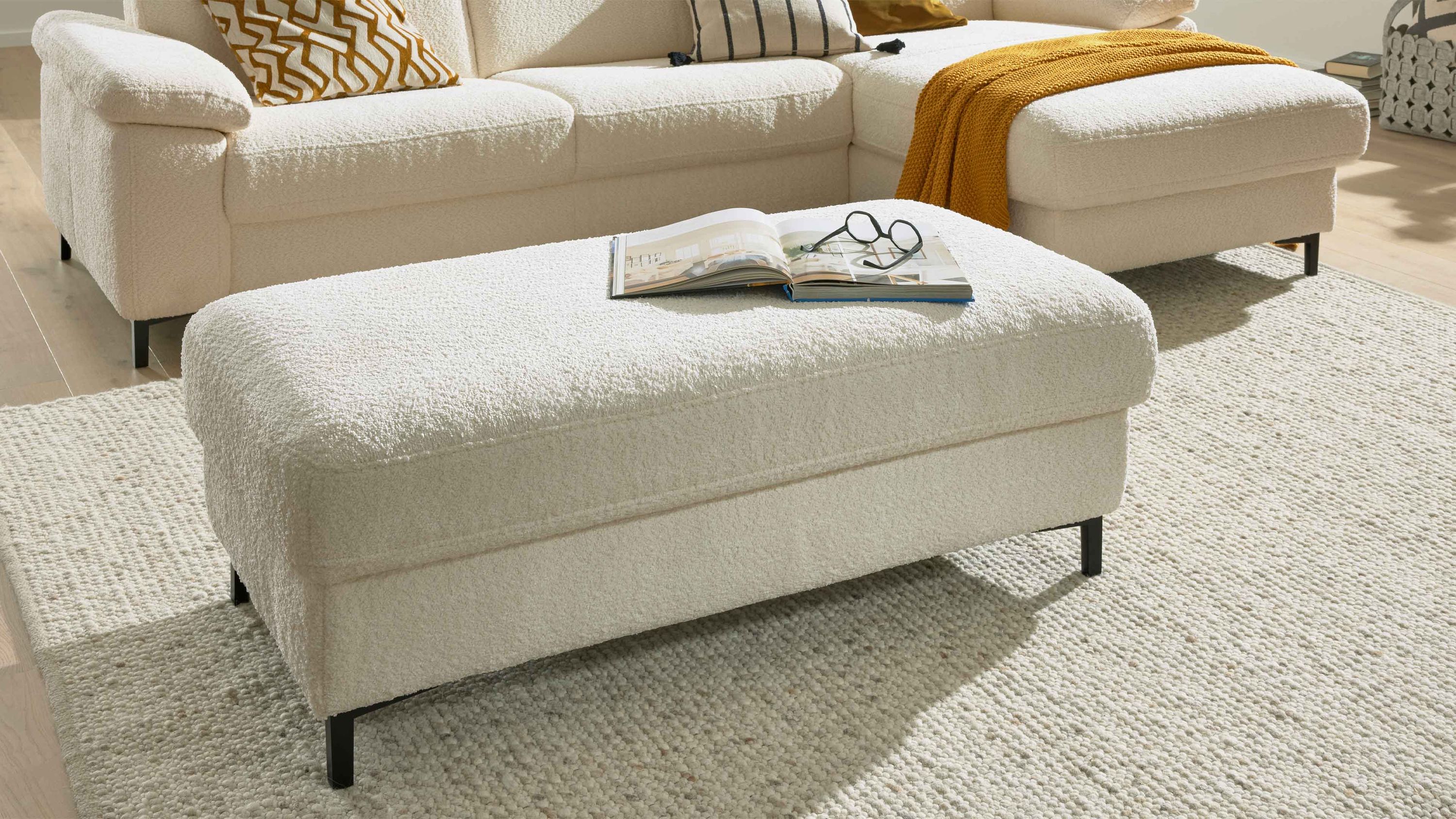 Rechteckiger Hocker mit naturweißem Stoffbezug und schwarzen Metallfüßen vor Sofa