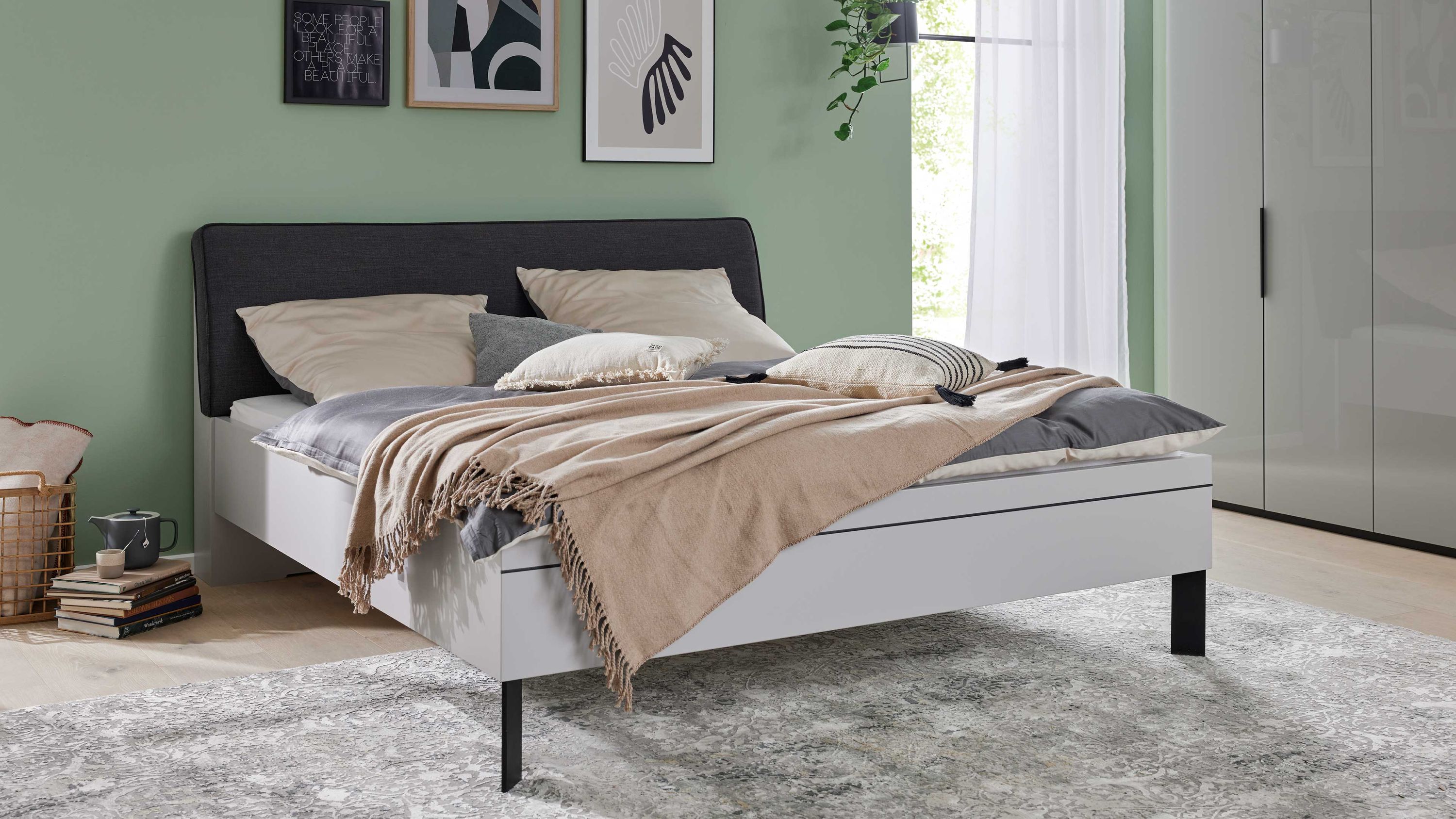 Bett mit weißem Rahmen und anthrazitfarbenem gepolstertem Kopfteil in modernem Schlafzimmer