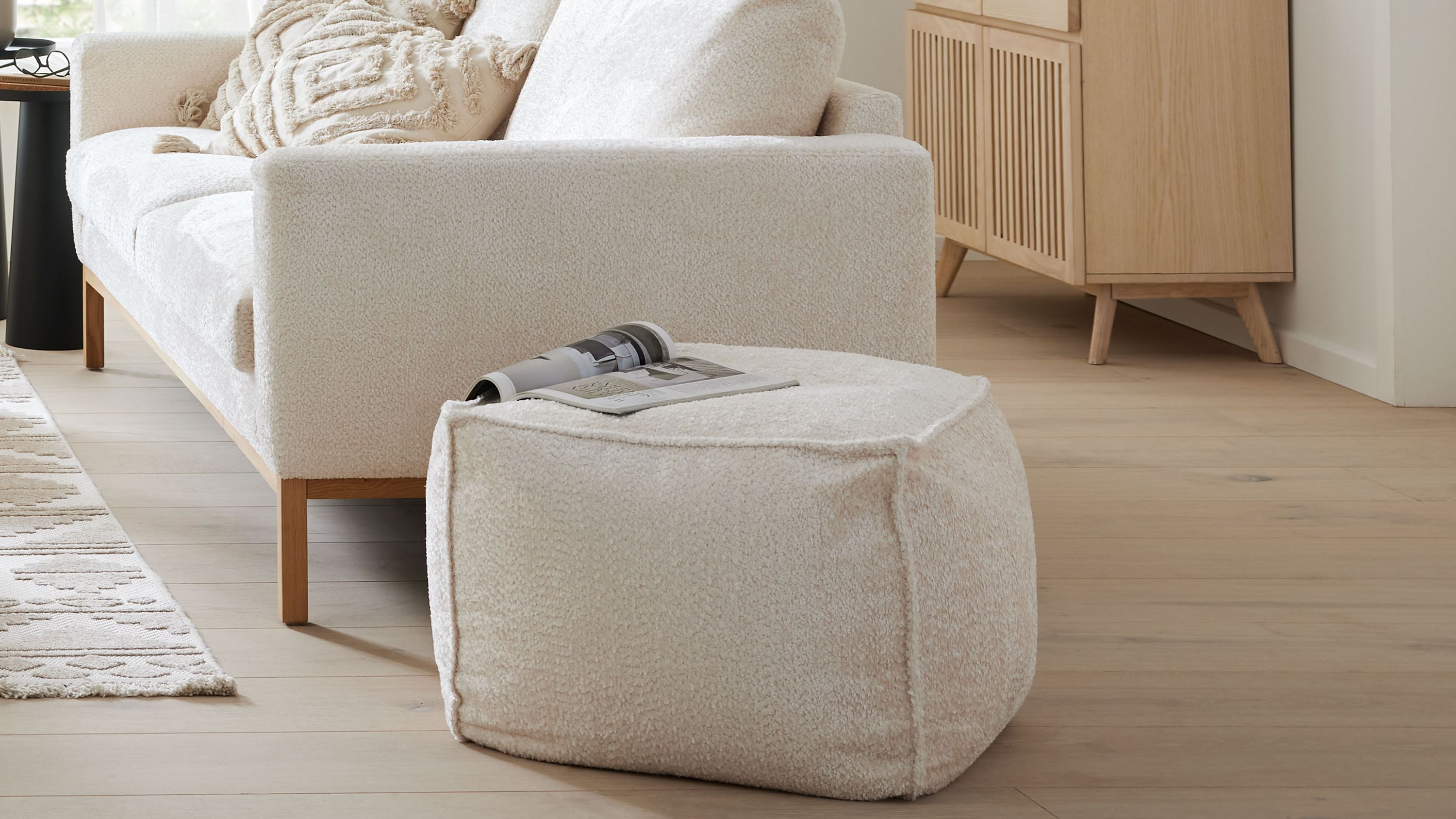 Weißer sechseckiger Hocker mit Stoffbezug in einem Wohnzimmer neben einem Sofa und einem Sideboard