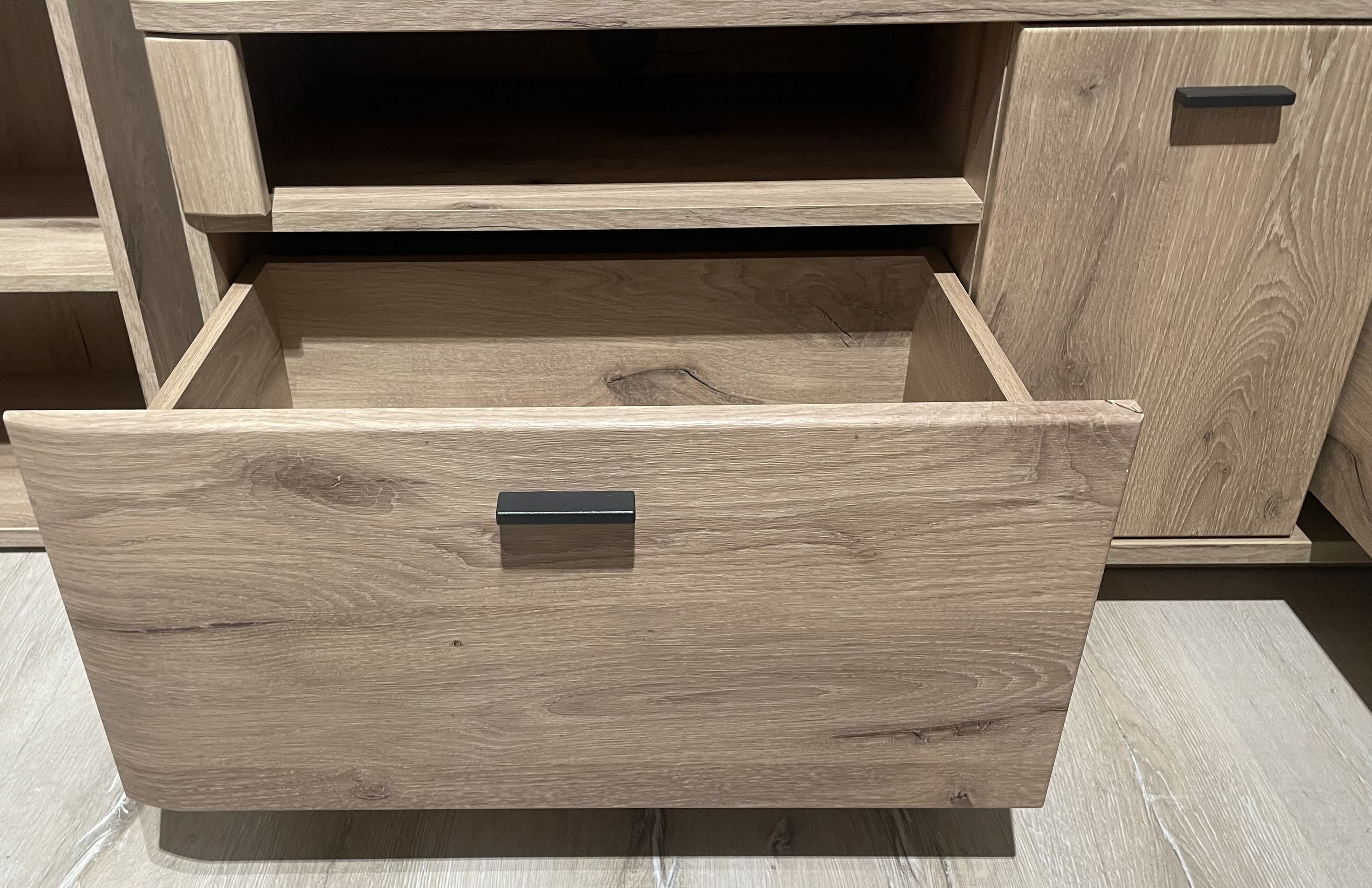 Offene Schublade einer Wohnwand in Holzoptik mit schwarzem Griff