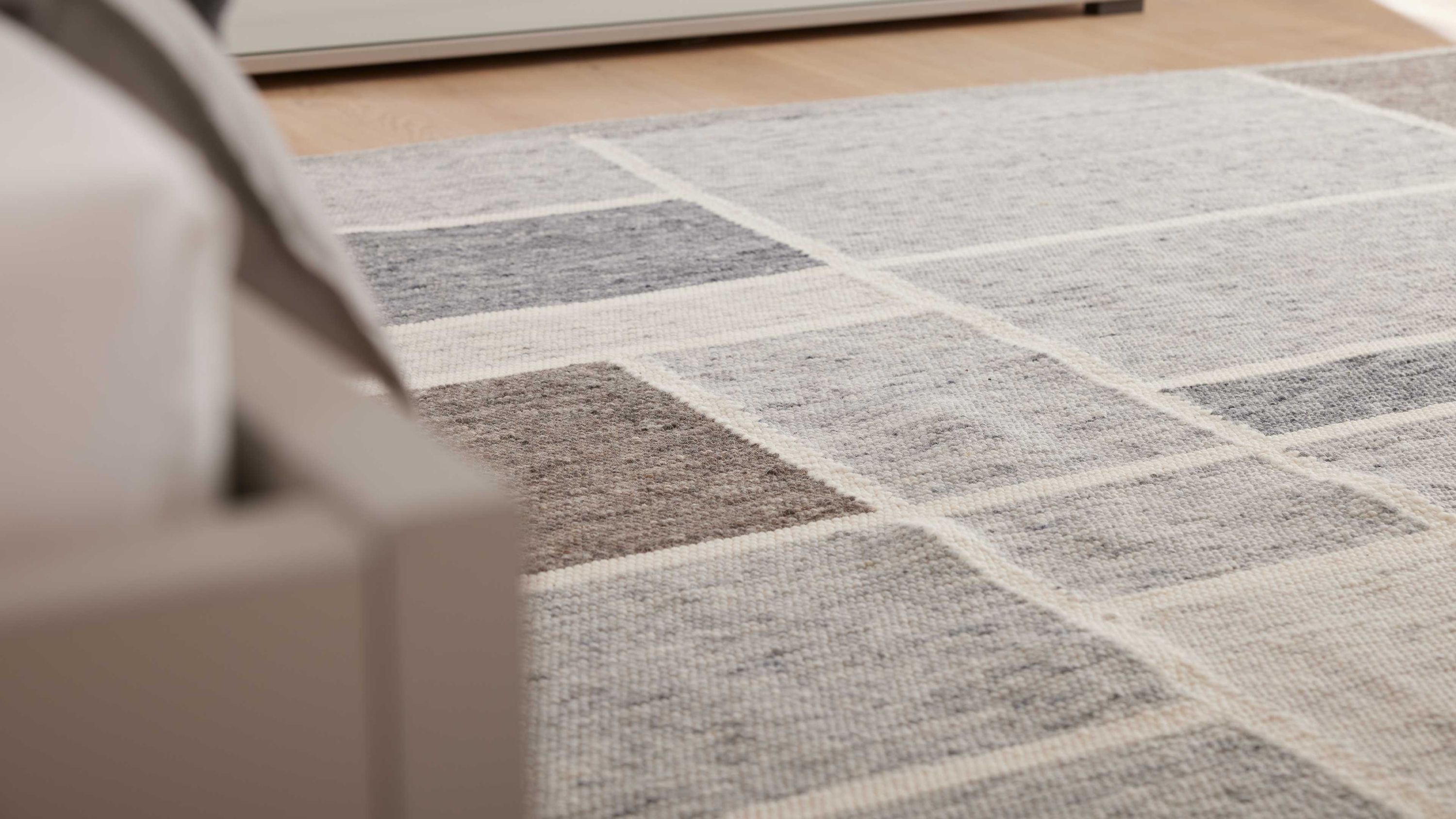 Rechteckiger Teppich mit geometrischem Muster aus grauen und hellgrauen Quadraten auf hellem Untergrund