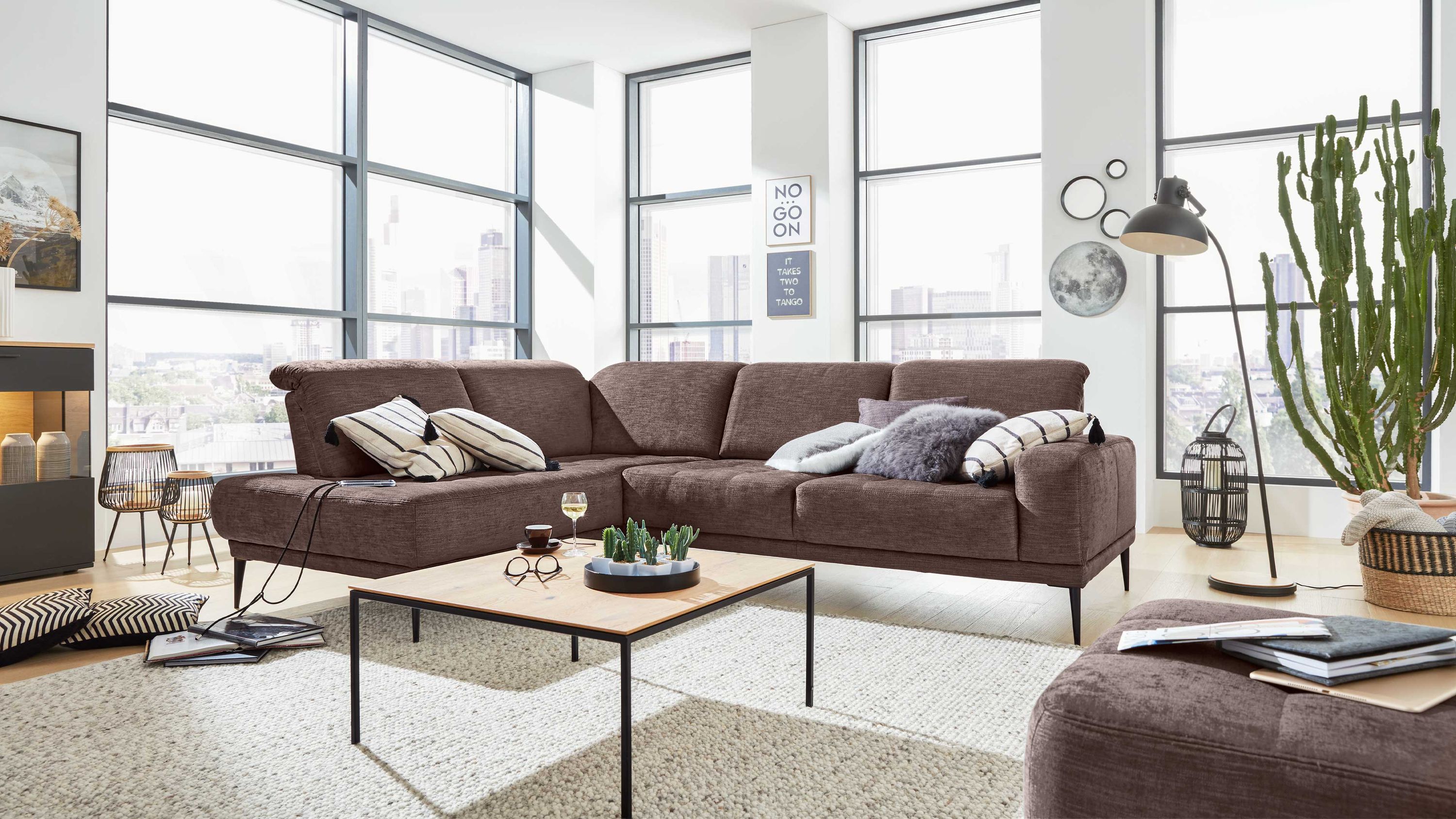 Braunes Ecksofa mit hohen Rückenlehnen und schwarzen Füßen in modernem Wohnzimmer mit großen Fenstern