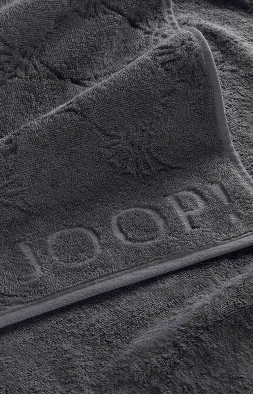 Nahaufnahme eines JOOP Duschtuchs in Anthrazit mit geprägtem Cornflower-Muster und diagonal verlaufendem JOOP Logo