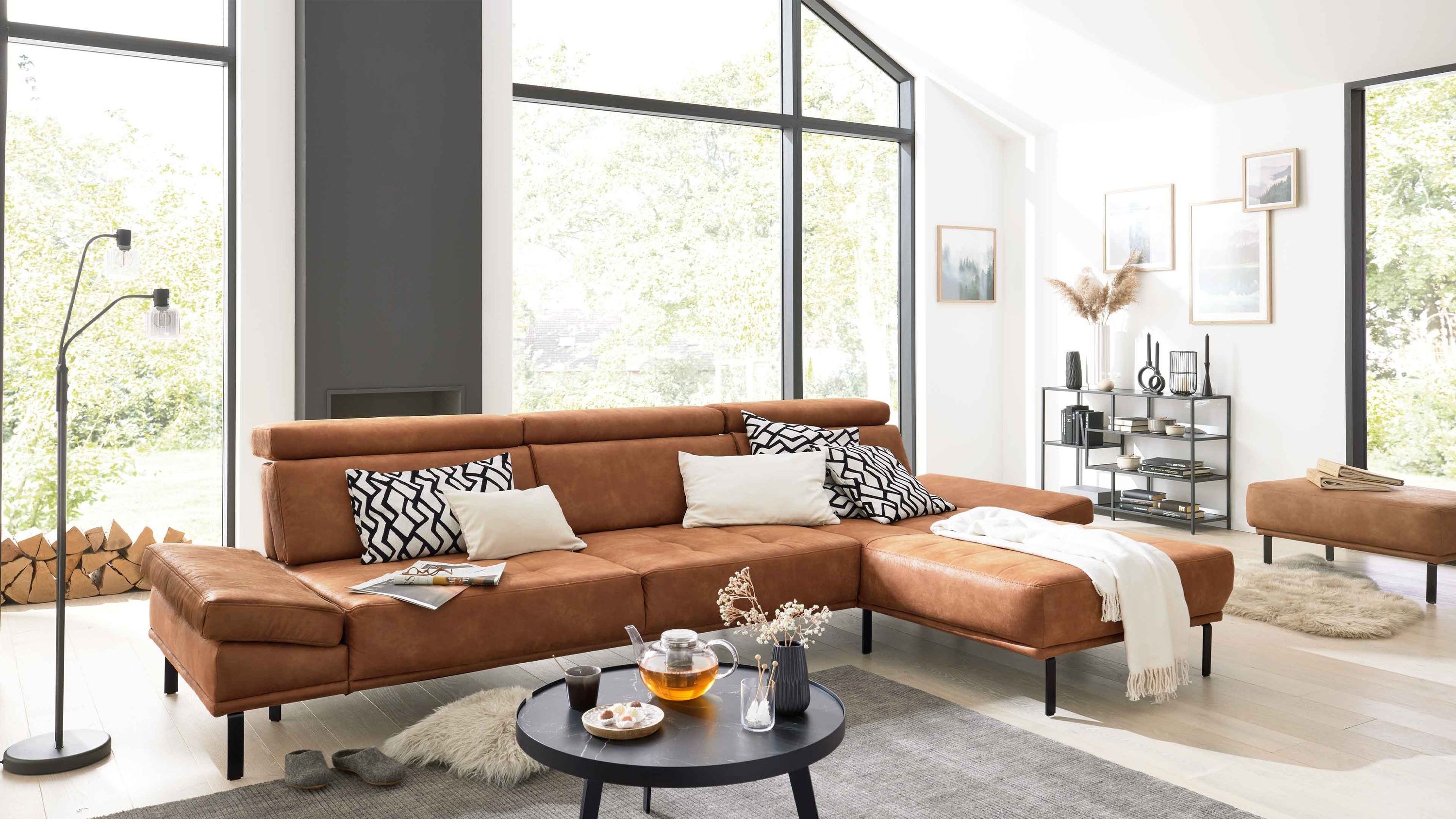Ecksofa mit tabacfarbenem Bezug und schwarzen Metallfüßen in modernem Wohnzimmer mit großen Fenstern