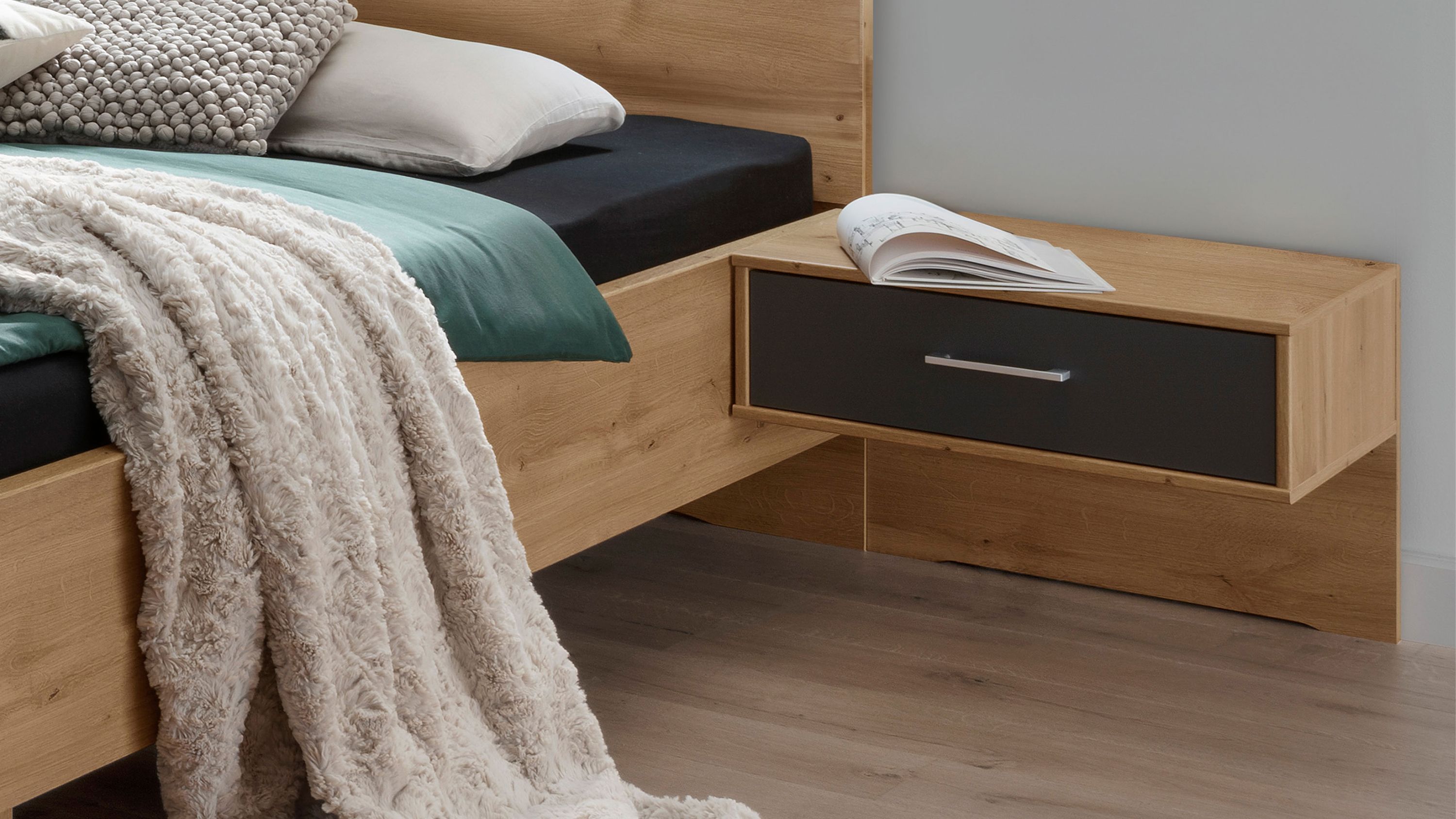 Zweiteiliges Nachtkonsolen-Set mit je einer Schublade in Holzoptik und dunkler Front wandhängend neben einem Bett