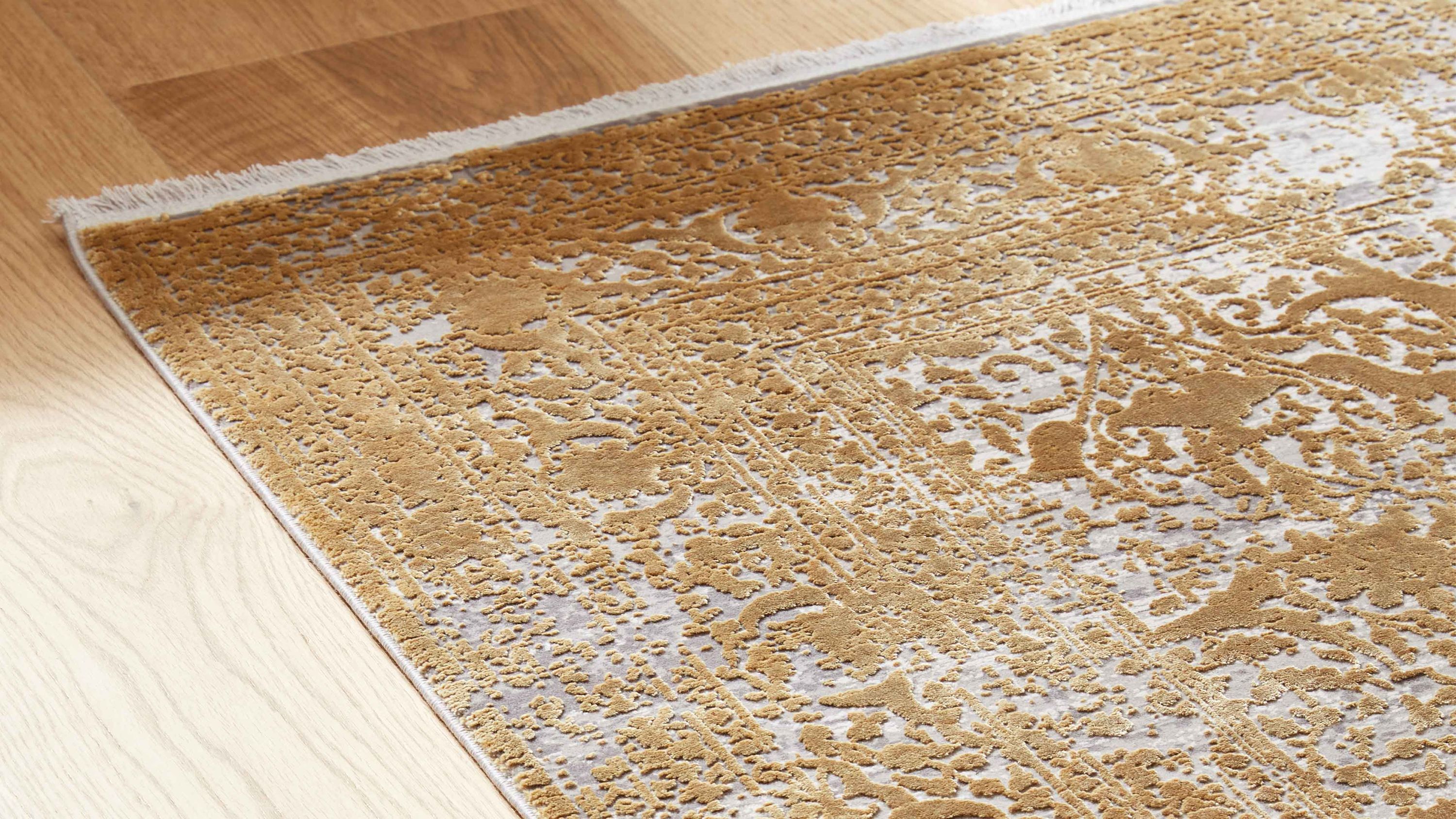 Rechteckiger Teppich mit floralen Mustern in gold und weiß auf hellem Boden