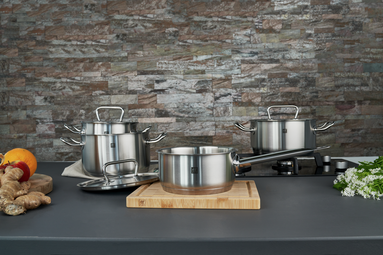 Edelstahl-Kochtöpfe und Stieltopf mit Deckeln auf Induktionskochfeld, moderne Küche mit Steinrückwand