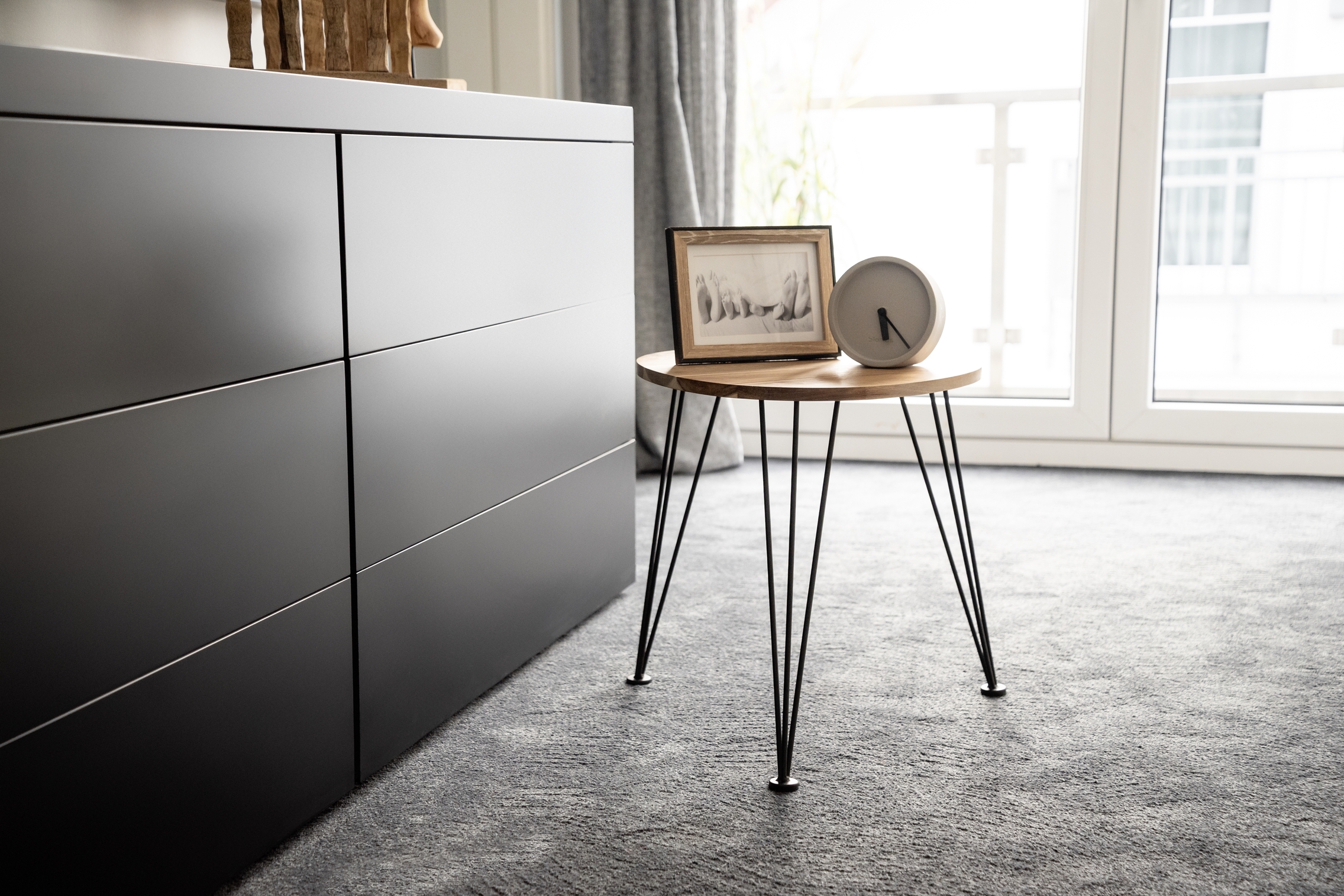 Beistelltisch, stabiles Dreieckdesign Beistelltisch mit Holzplatte und Metallbeinen neben schwarzer Kommode auf Teppich mit Rahmen und Dekoobjekt