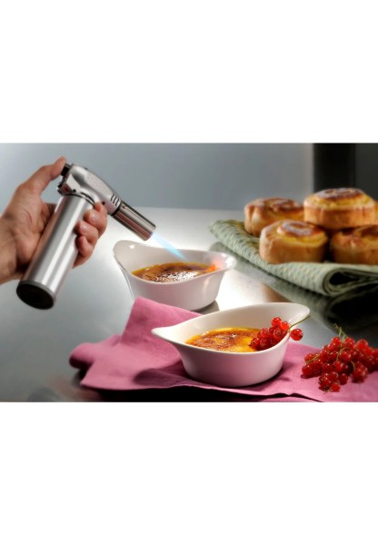 Crème Brûlée flambieren Aus schräger Perspektive: Hand karamellisiert Crème Brûlée mit Brenner, weitere Schale und Gebäck im Hintergrund