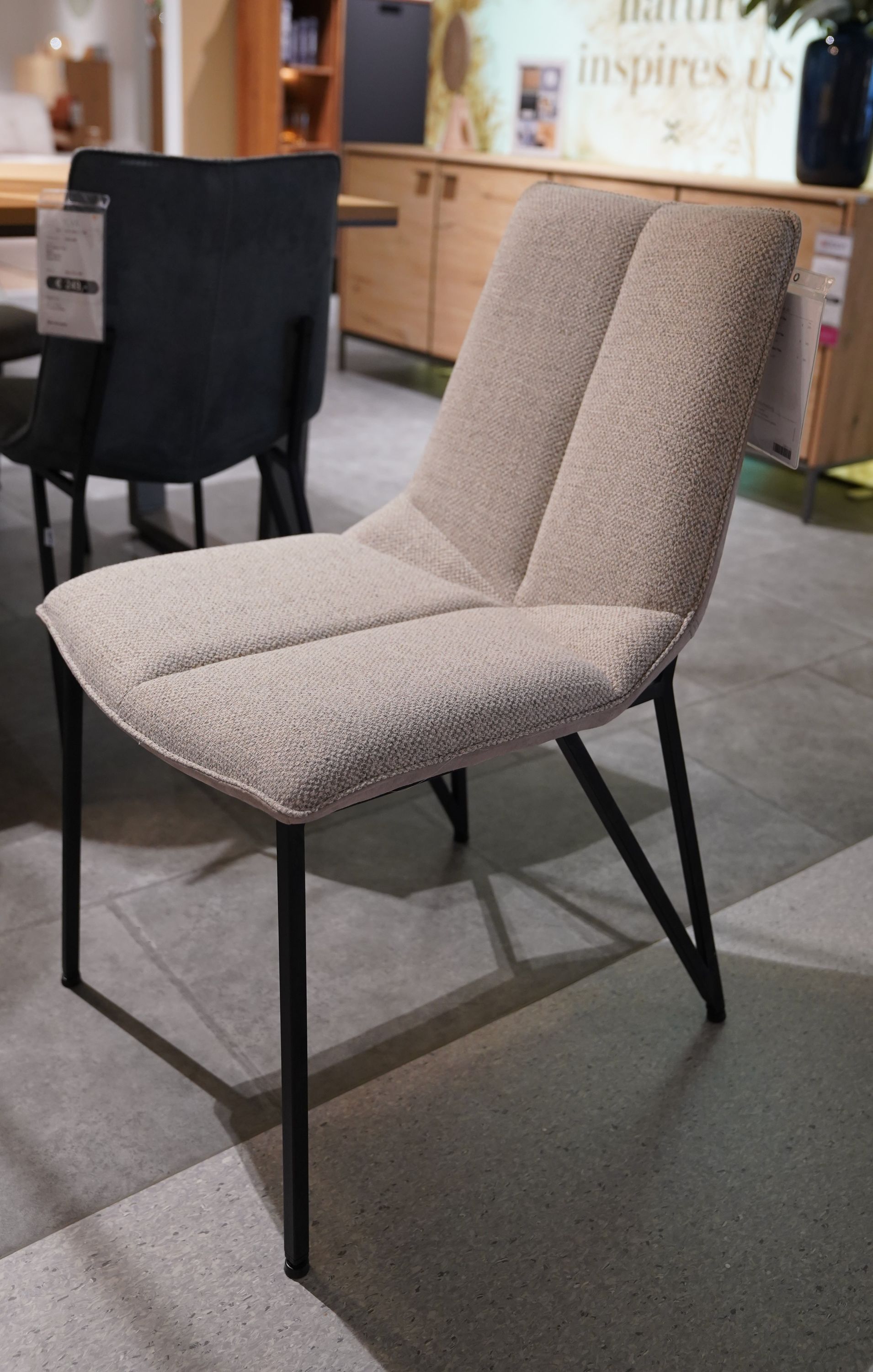 Beiger Stuhl Ylva mit gepolsterter Sitzfläche und Rückenlehne, schwarzen Metallbeinen und modernem, kantigem Design.