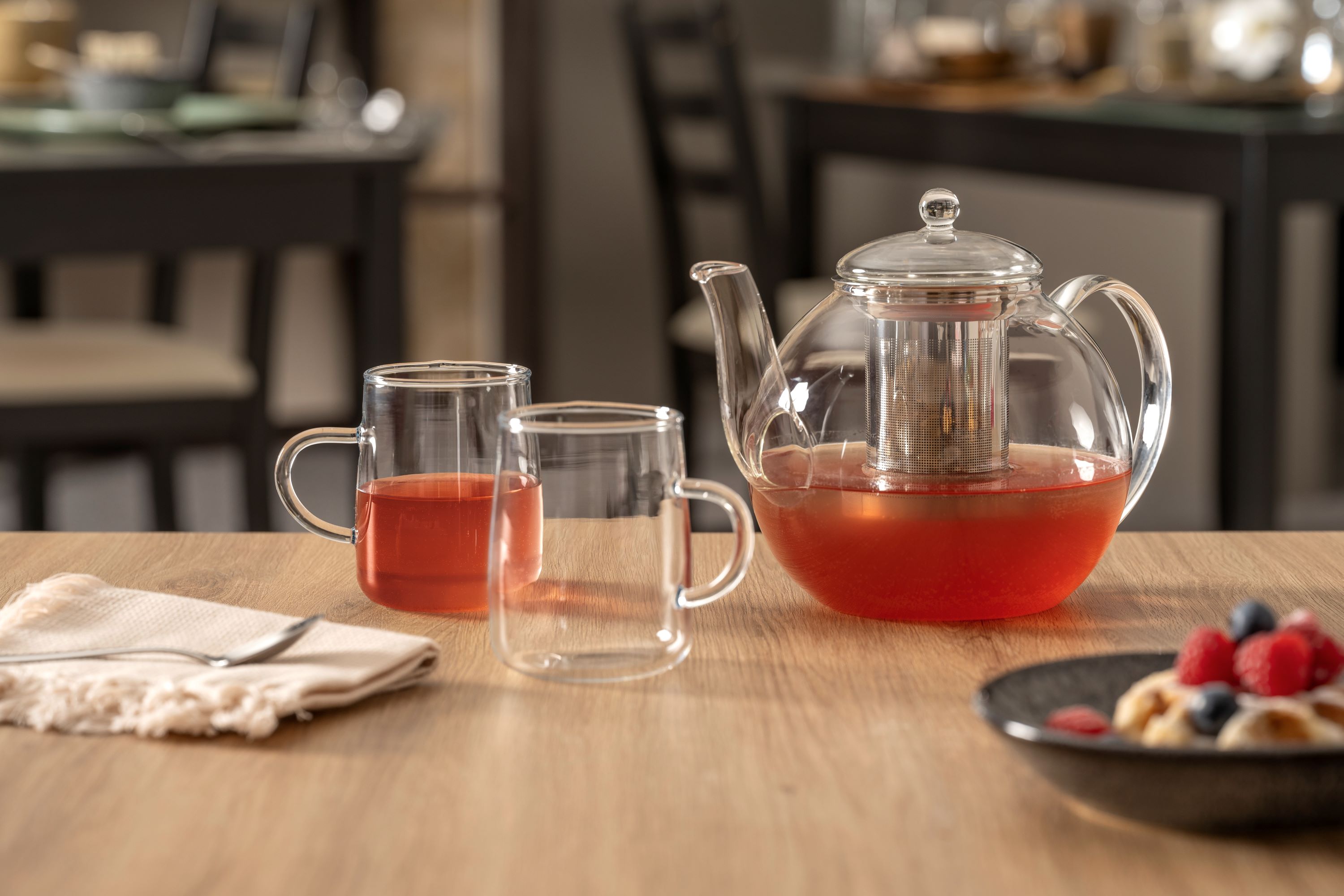 Glaskanne mit Teesieb und zwei Glastassen mit rotem Tee auf Holztisch