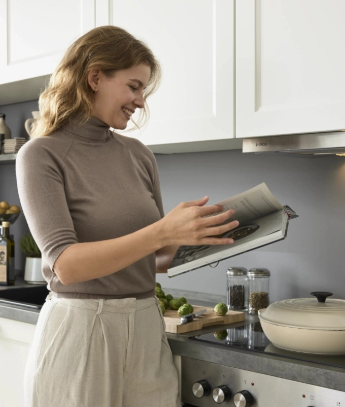 Frau mit Kochbuch in moderner Küche Junge Frau liest in Kochbuch vor Küchenzeile mit Einbaugeräten und grauen Fronten