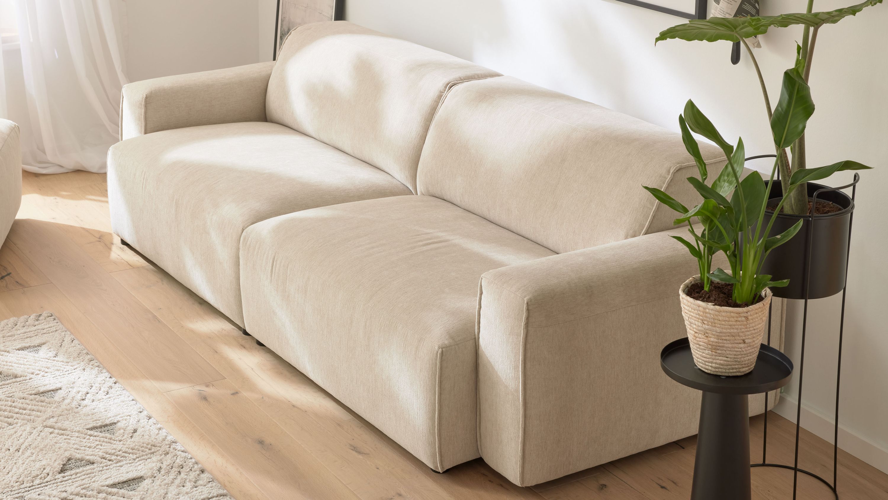 Zweisitziges Sofa mit champagnerfarbenem Stoffbezug und breiten Armlehnen in hellem Wohnraum