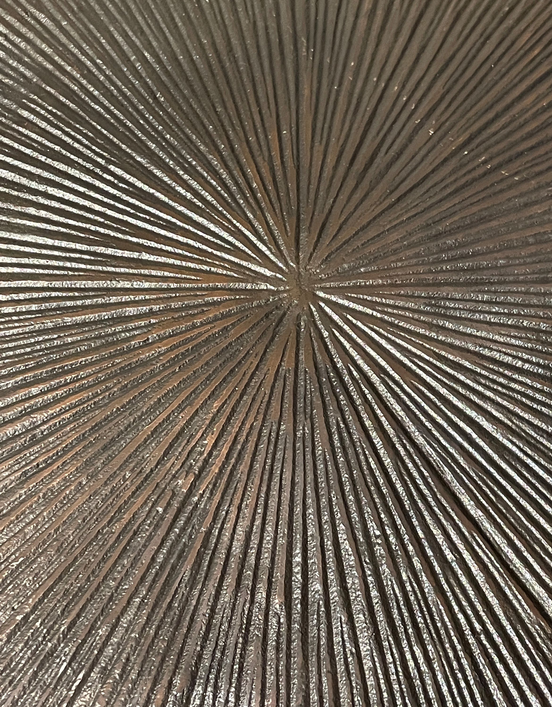 Nahaufnahme einer strukturierten, radial gemusterten Metalloberfläche in dunkler Bronzeoptik.