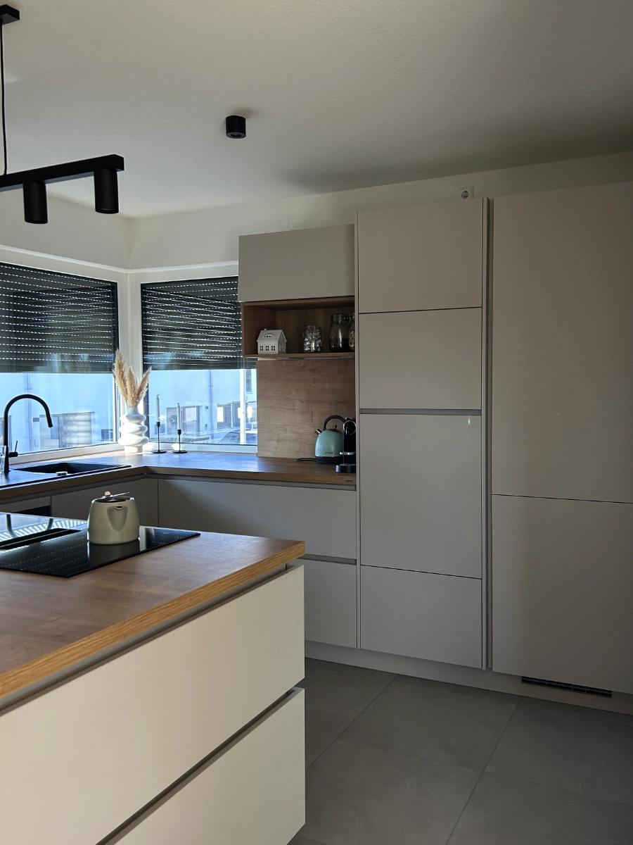 Moderne Wohnküche mit grauer Kochinsel, Holzarbeitsplatte, Induktionskochfeld, Spüle, Hängelampe und großen Fenstern.