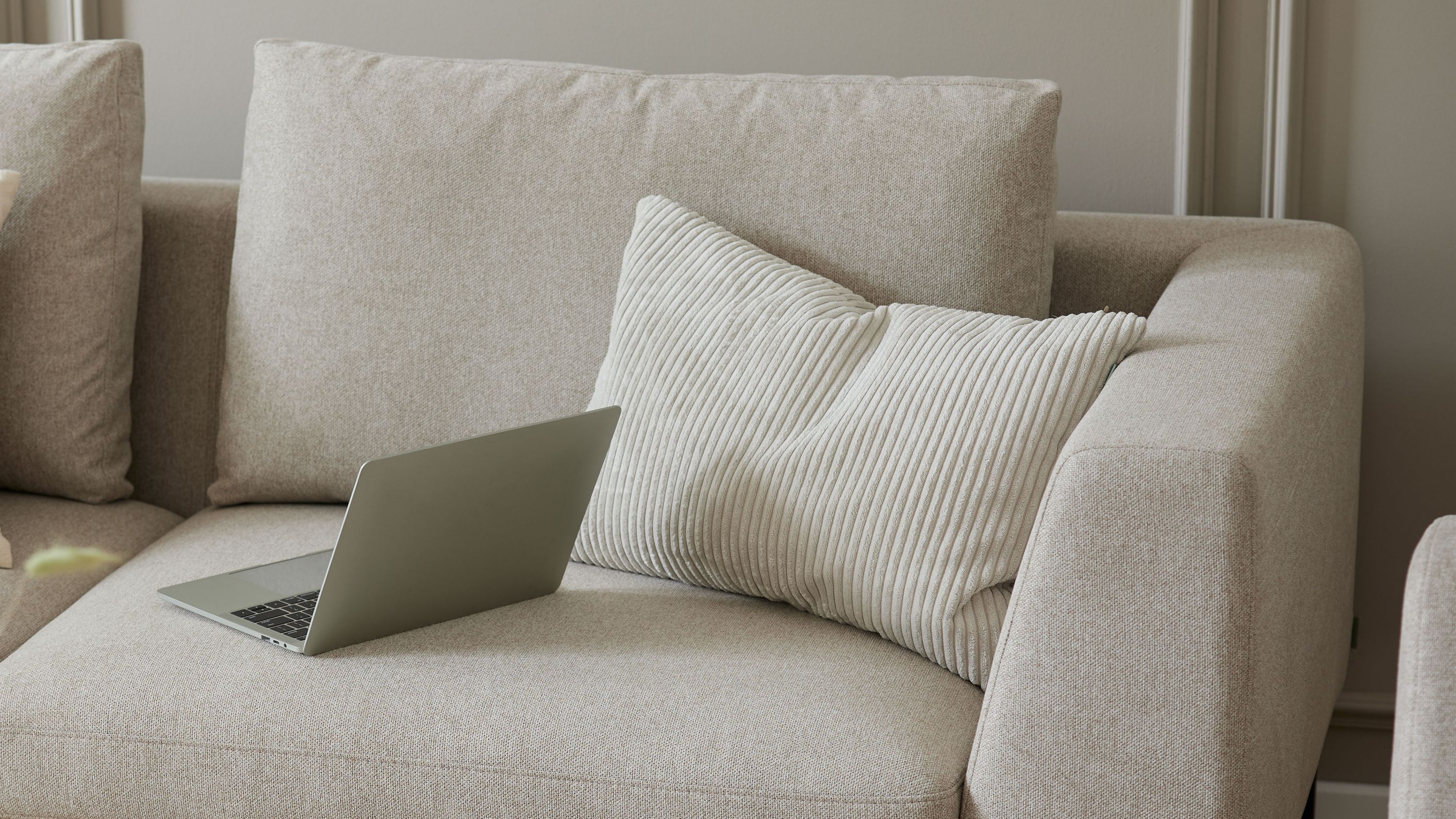 Beige Kissenhülle mit breiten Streifen auf einem hellen Sofa mit Laptop