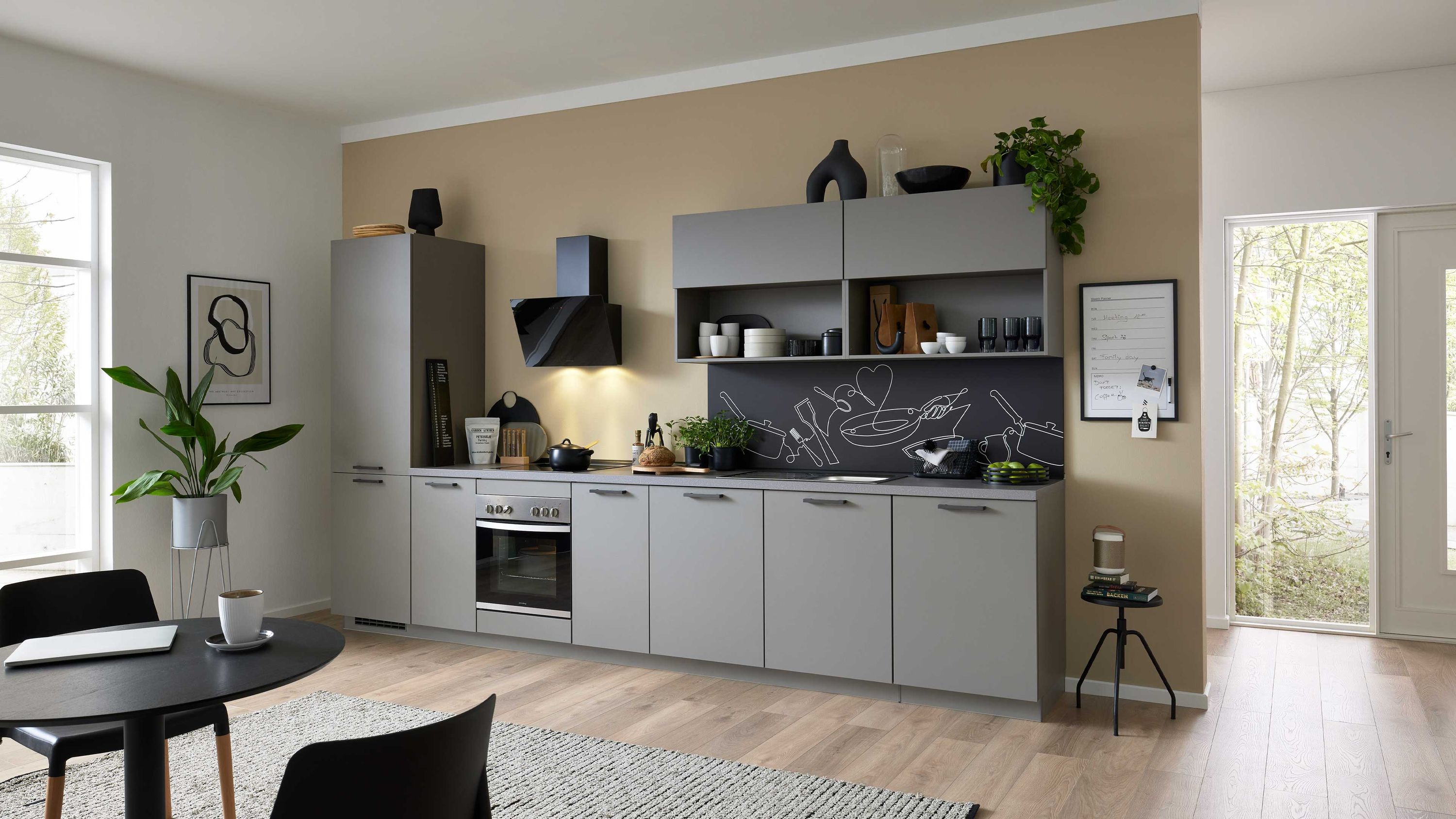 Graue Küche mit Kreidetafel-Rückwand offenen Regalen Pflanzen Einbauofen Tageslicht Esstisch im Vordergrund