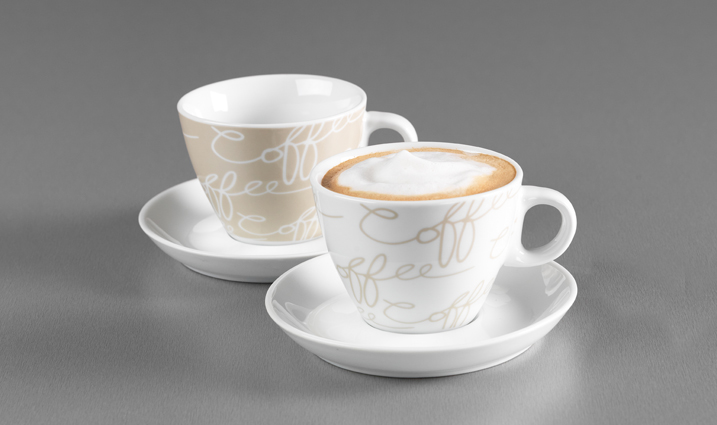 Zwei Cappuccinotassen mit Untertassen in Weiß und Creme mit Schriftzug auf grauem Hintergrund