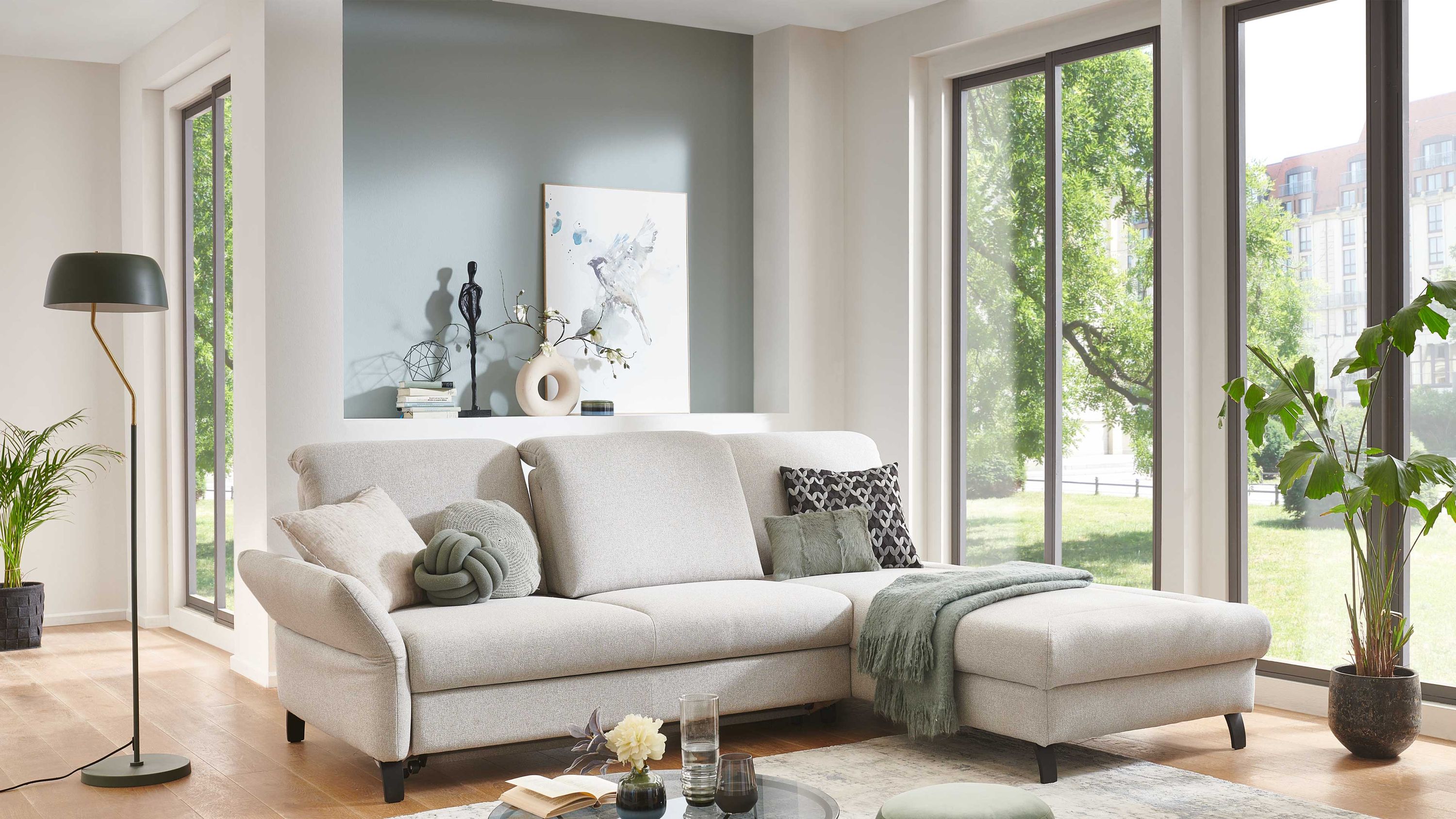 Ecksofa mit silberfarbenem Bezug und Metallfüßen Ecksofa mit silberfarbenem Bezug und Metallfüßen in hellem Wohnzimmer mit großen Fenstern