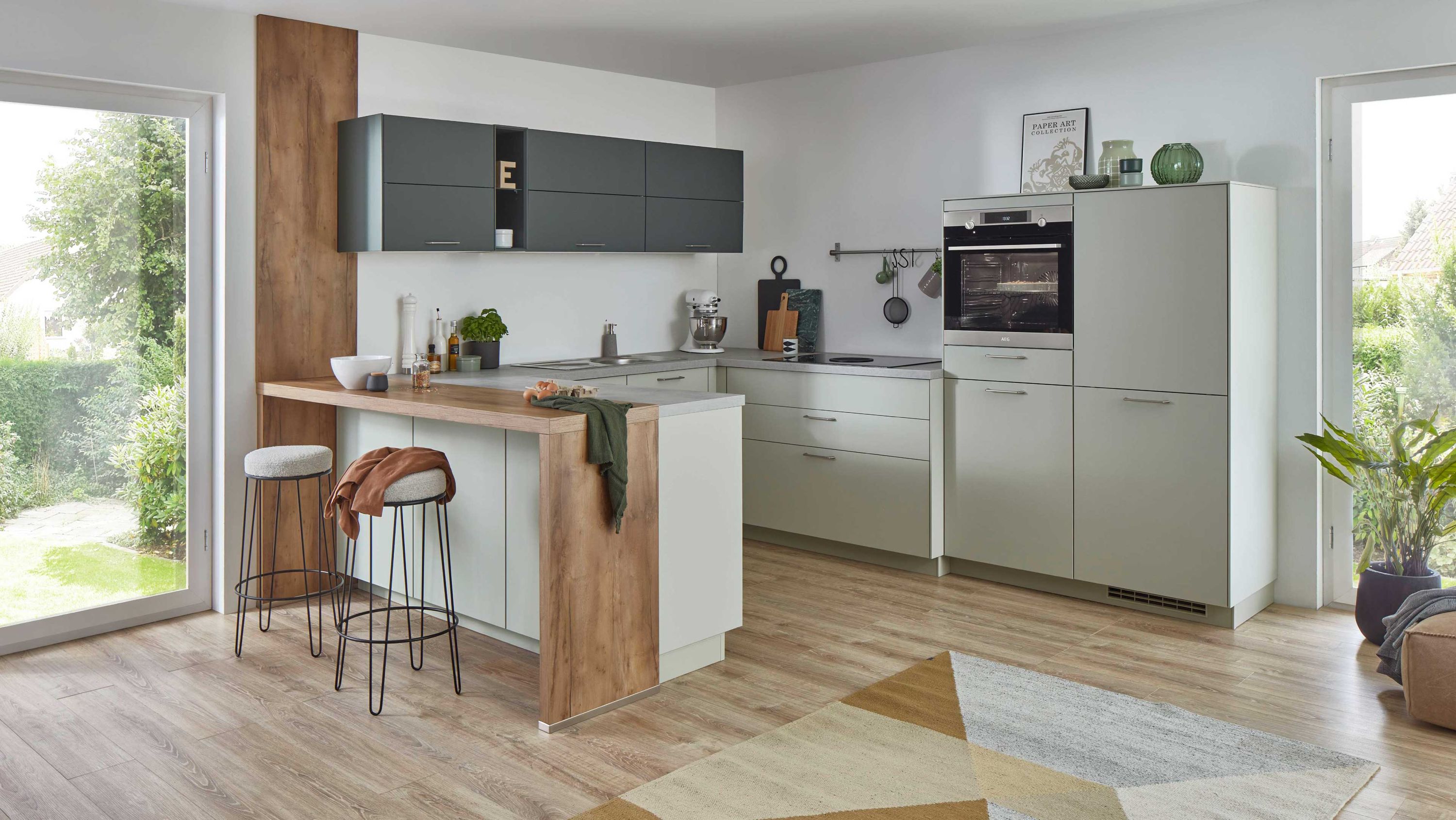 Moderne Winkelküche in Hellgrau mit Holzbar schwarzen Hängeschränken Einbauofen und großem Fensterblick.