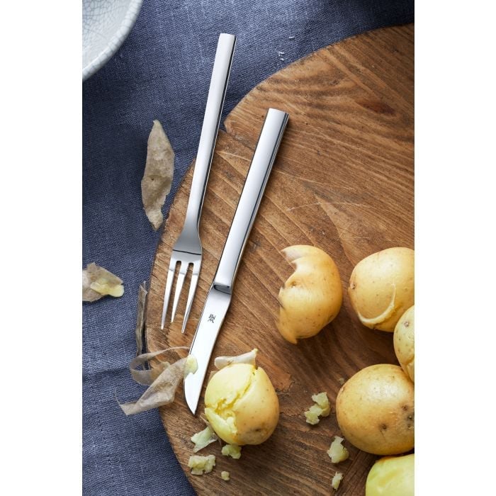 Pellkartoffelgabel und Schälmesser auf Holzbrett mit Pellkartoffeln und Schalen auf blauem Stoff fotografiert
