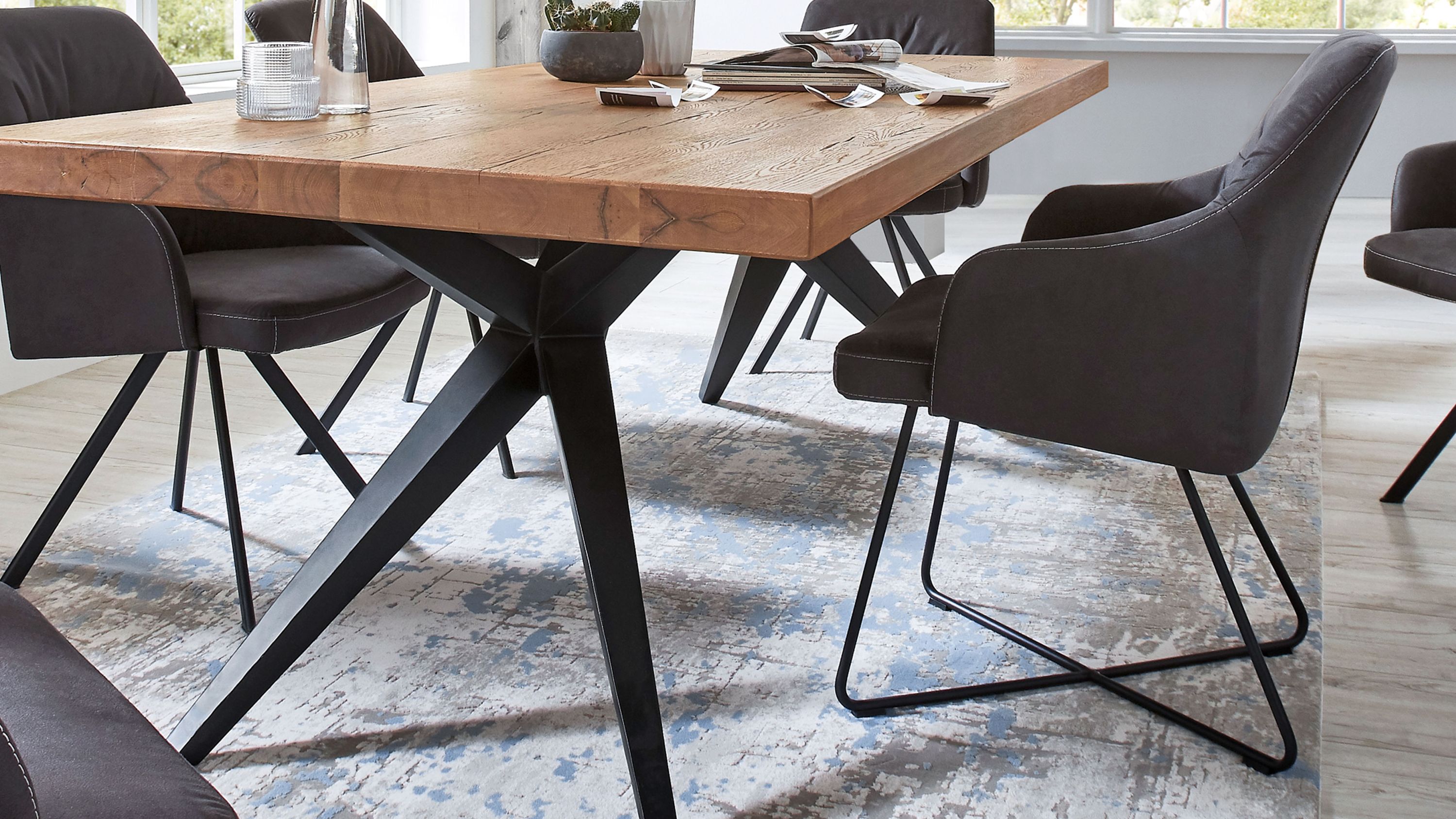 Armlehnstuhl mit anthrazitfarbener Polsterung und Metallgestell Armlehnstuhl mit anthrazitfarbener Polsterung und schwarzem Metallgestell neben Holztisch