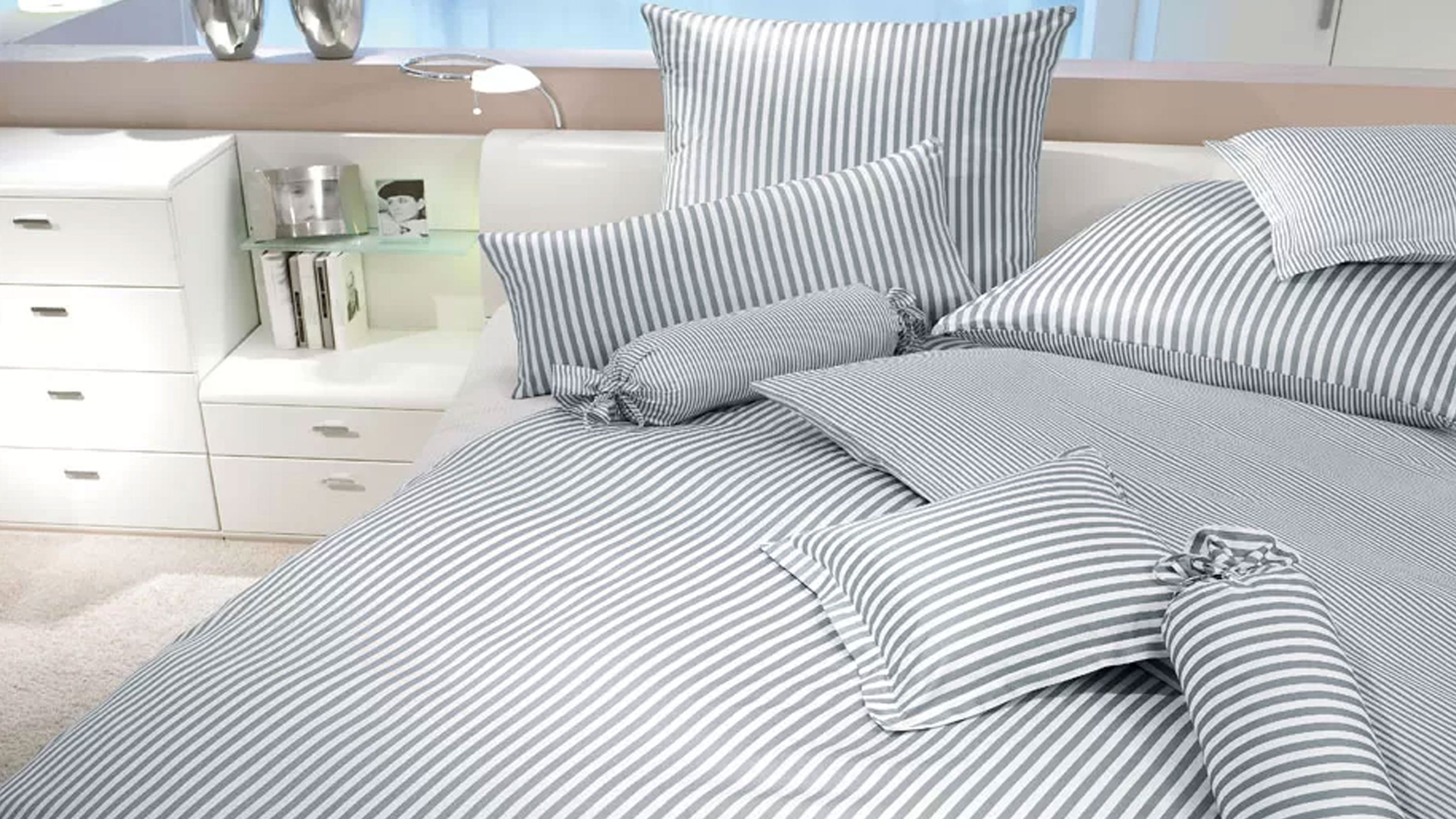 Bett mit grauer und weißer gestreifter Bettwäsche und mehreren Kissen in verschiedenen Formen
