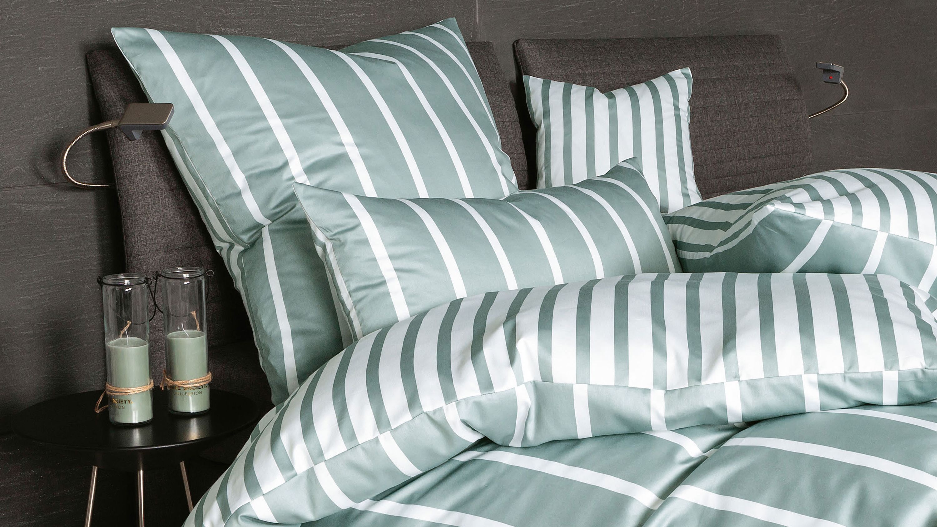 Bett mit gestreifter Bettwäsche in grün und weiß mit mehreren Kissen und Decke