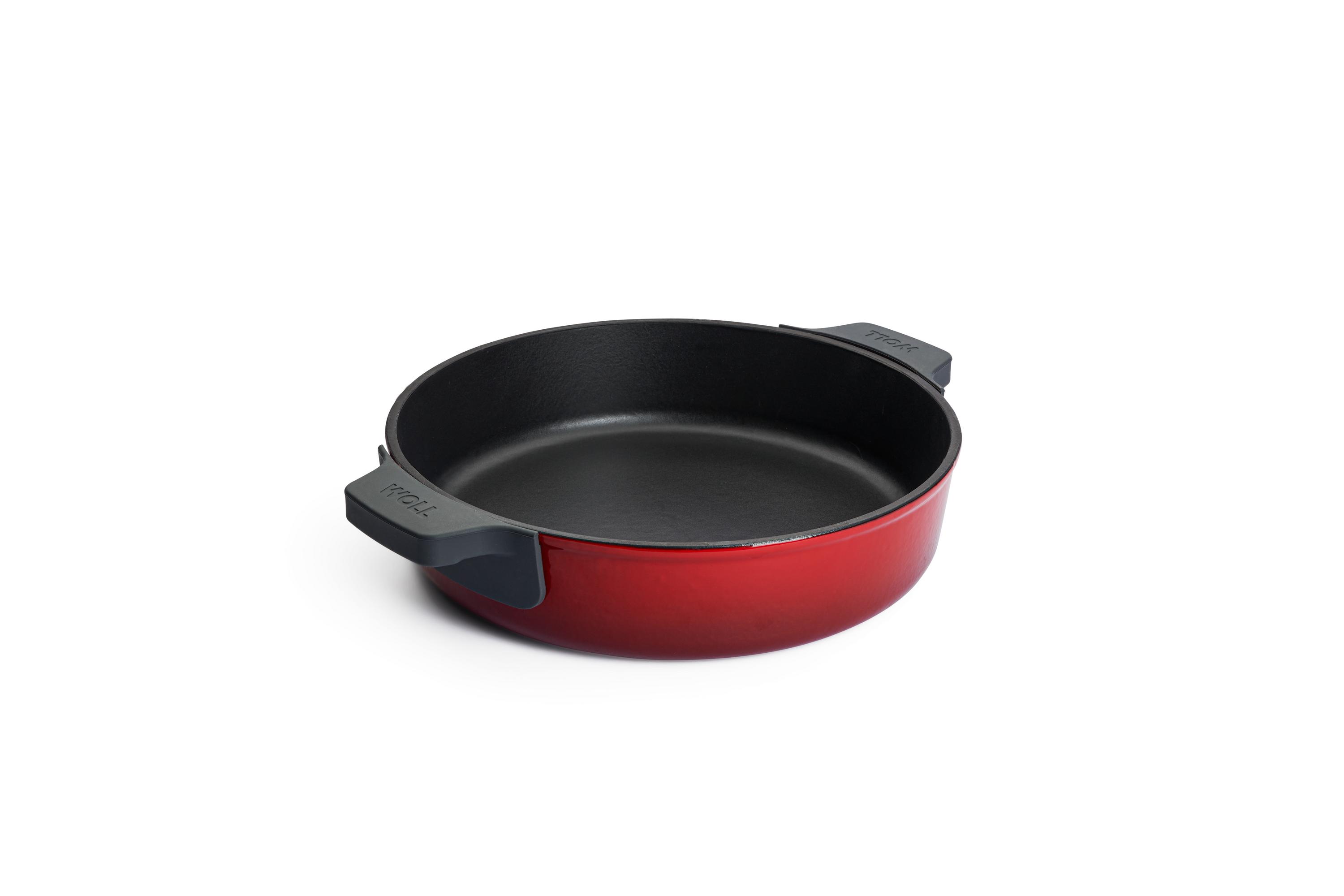 Chilli-roter Kochtopf ohne Deckel mit zwei schwarzen Griffen leicht erhöht von links fotografiert auf heller Oberfläche