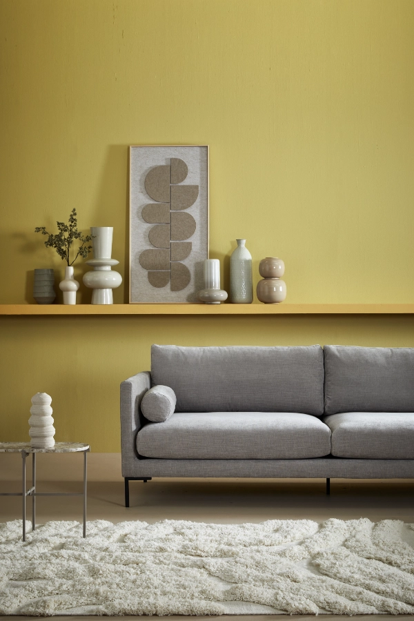 Nahaufnahme eines modernen Wohnzimmers mit gelber Wand, grauem Sofa, Couchtisch und Regalen.