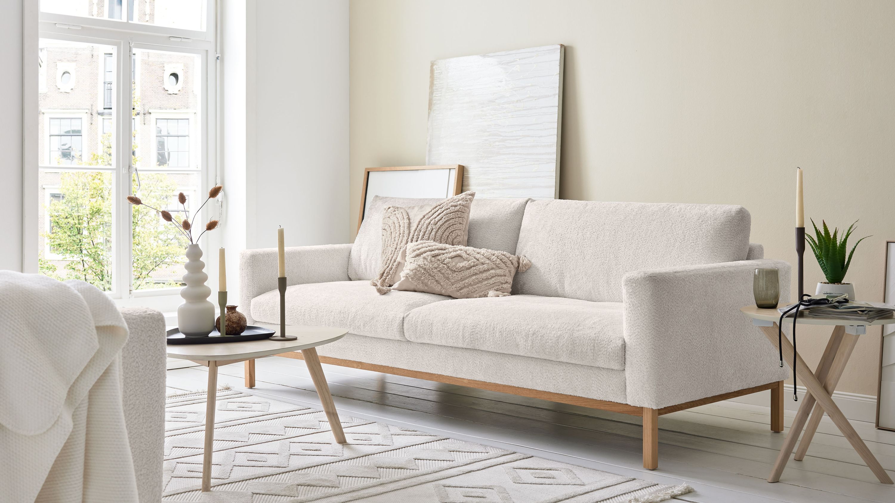 Bigsofa mit weißem Stoffbezug und Holzfüßen Bigsofa mit weißem Stoffbezug Holzfüßen und zwei dekorativen Kissen in hellem Wohnzimmer