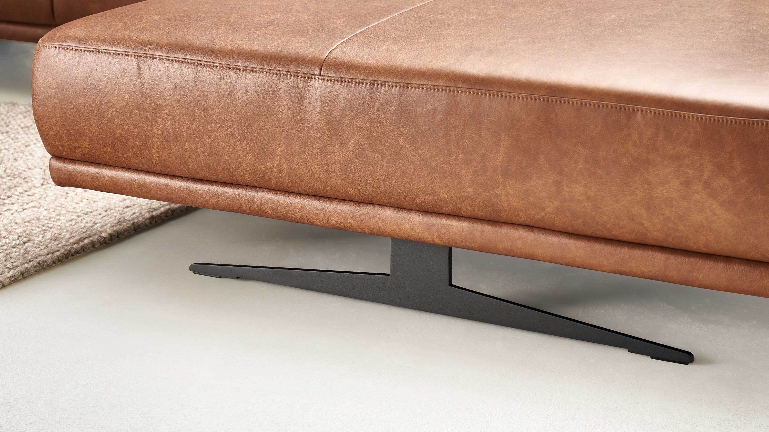 Schwertkufenfuß aus mattschwarzem Metall unter braunem Polstersofa