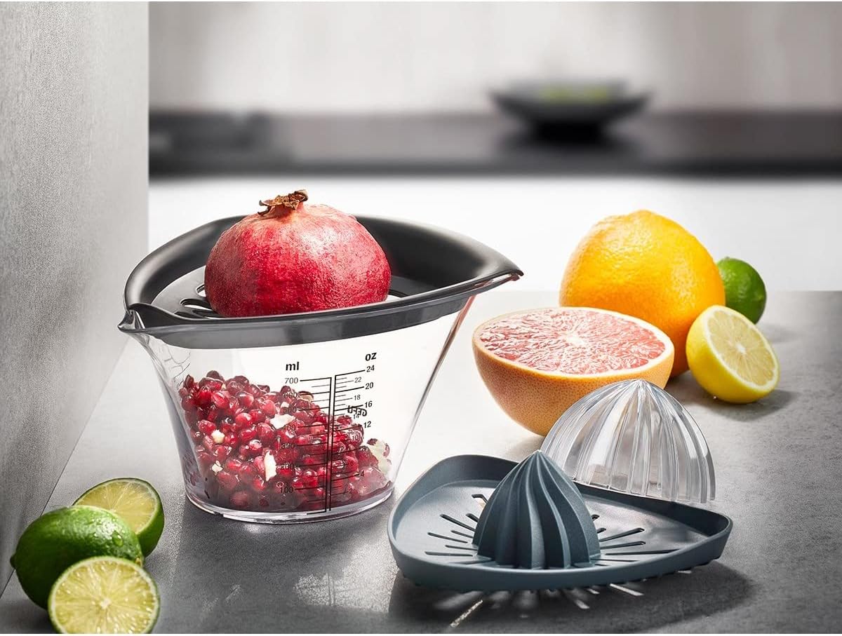Küchenszene mit Granatapfelentkerner halber Frucht Zitrusfrüchten und grauer Zitruspresse aus Frontperspektive
