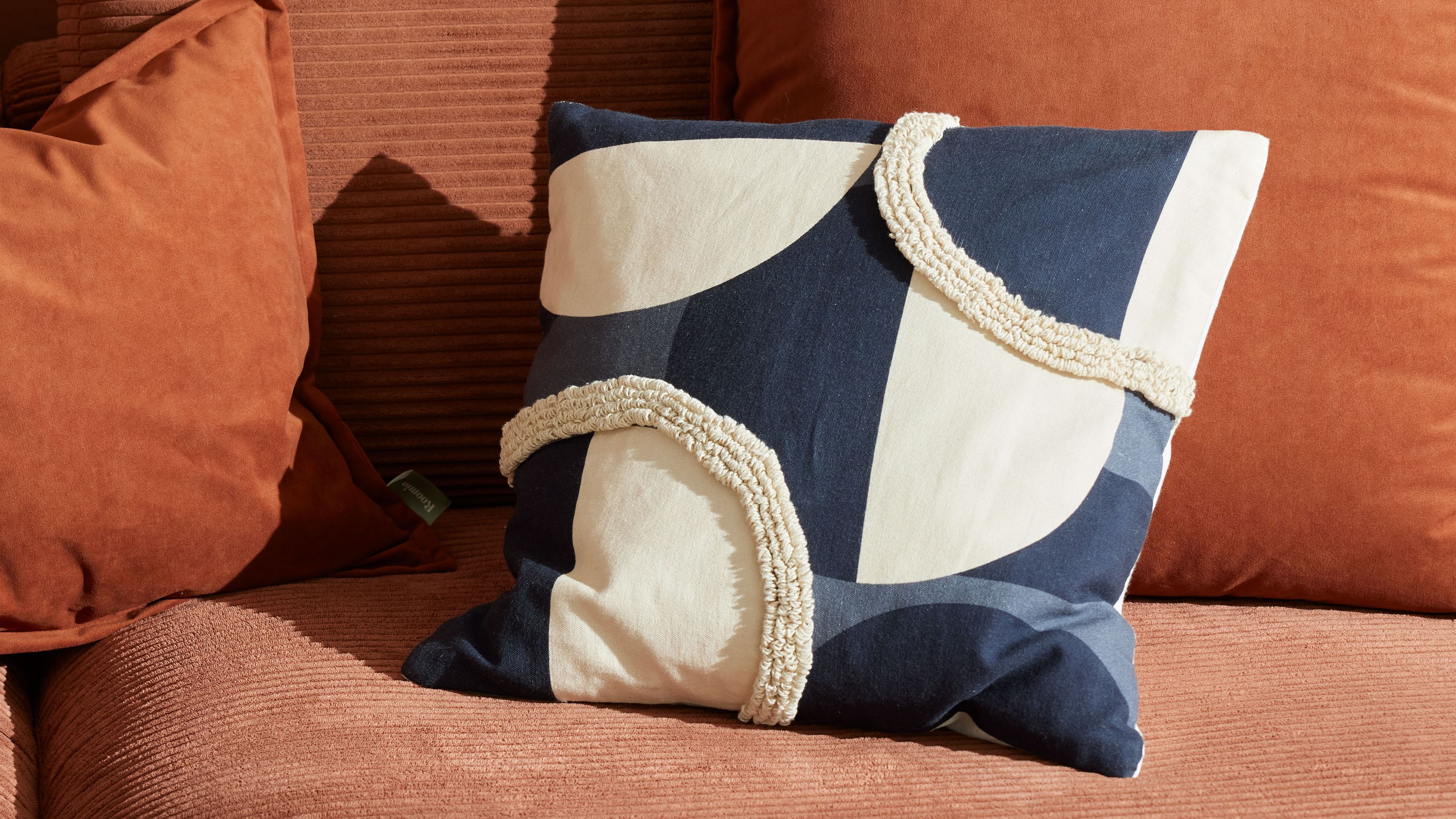 Quadratisches Kissen mit blau-weißem geometrischem Muster und weißen Fransen auf braunem Sofa