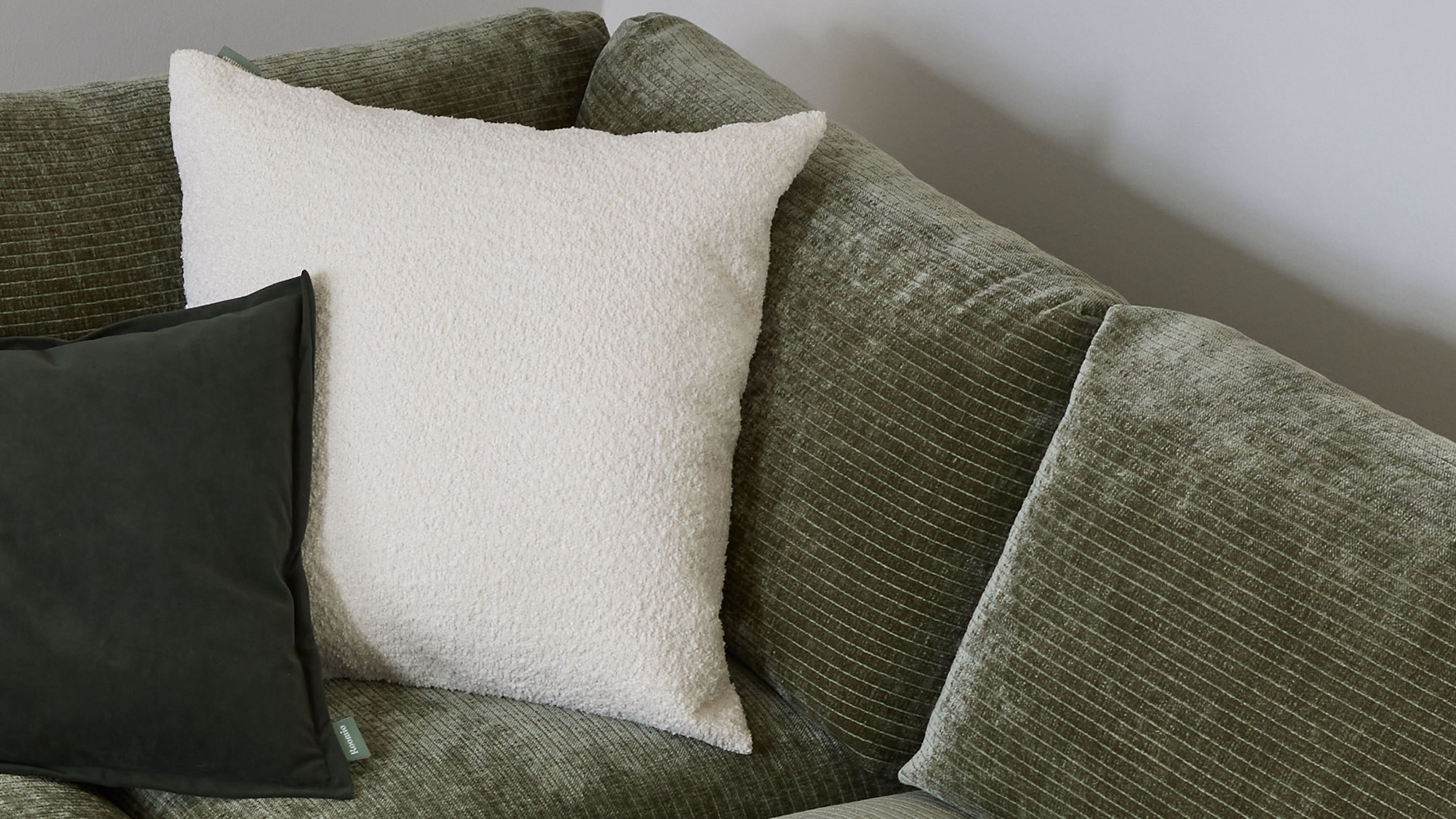 Weiße quadratische Kissenhülle auf grünlichem Sofa Quadratische weiße Kissenhülle mit strukturierter Oberfläche auf grünlichem Sofa