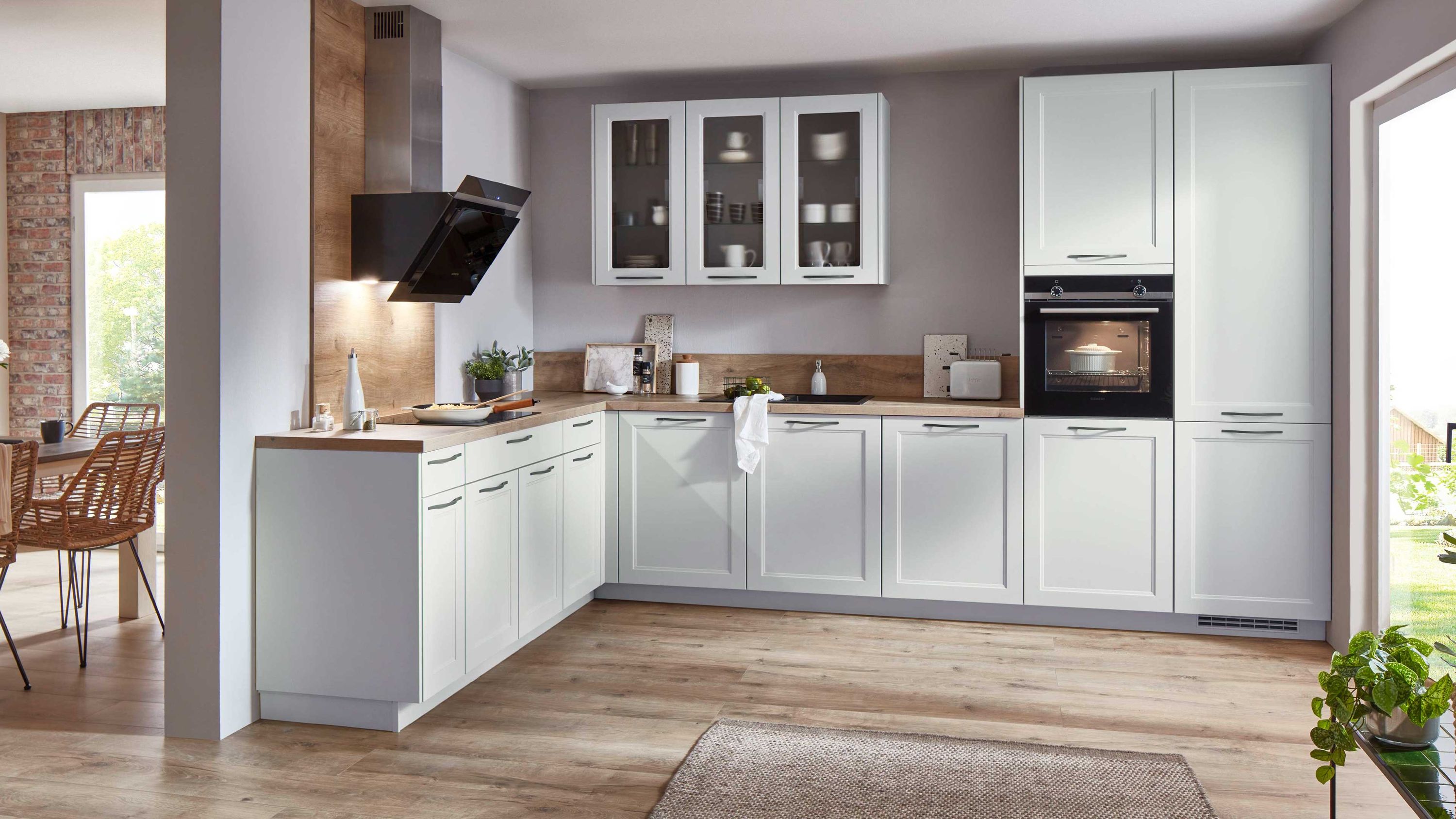 Landhaus-L-Küche in Weiß mit Holzarbeitsplatte. Helle L-Küche im Landhausstil mit Glashängeschränken Holzarbeitsplatte Einbauofen und schwarzer Dunstabzugshaube.