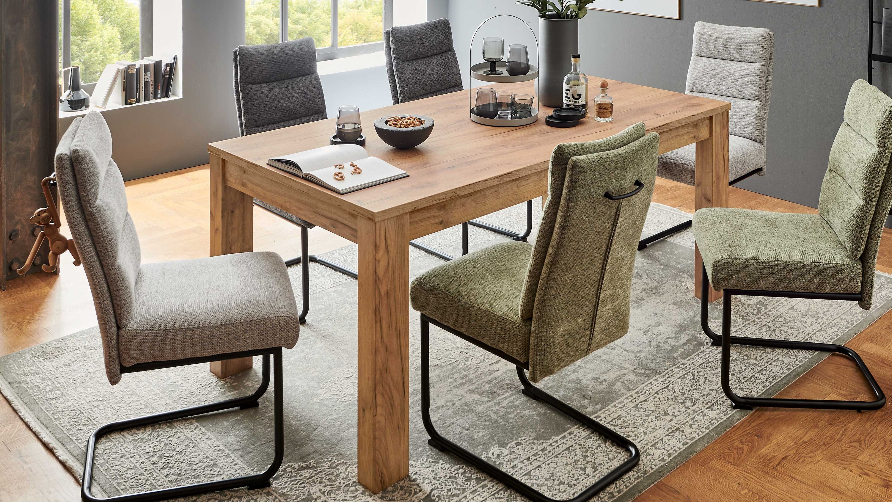 Ausziehtisch in terrafarbener Holzoptik mit sechs gepolsterten Stühlen in Grau und Grün auf Teppich im modernen Esszimmer.
