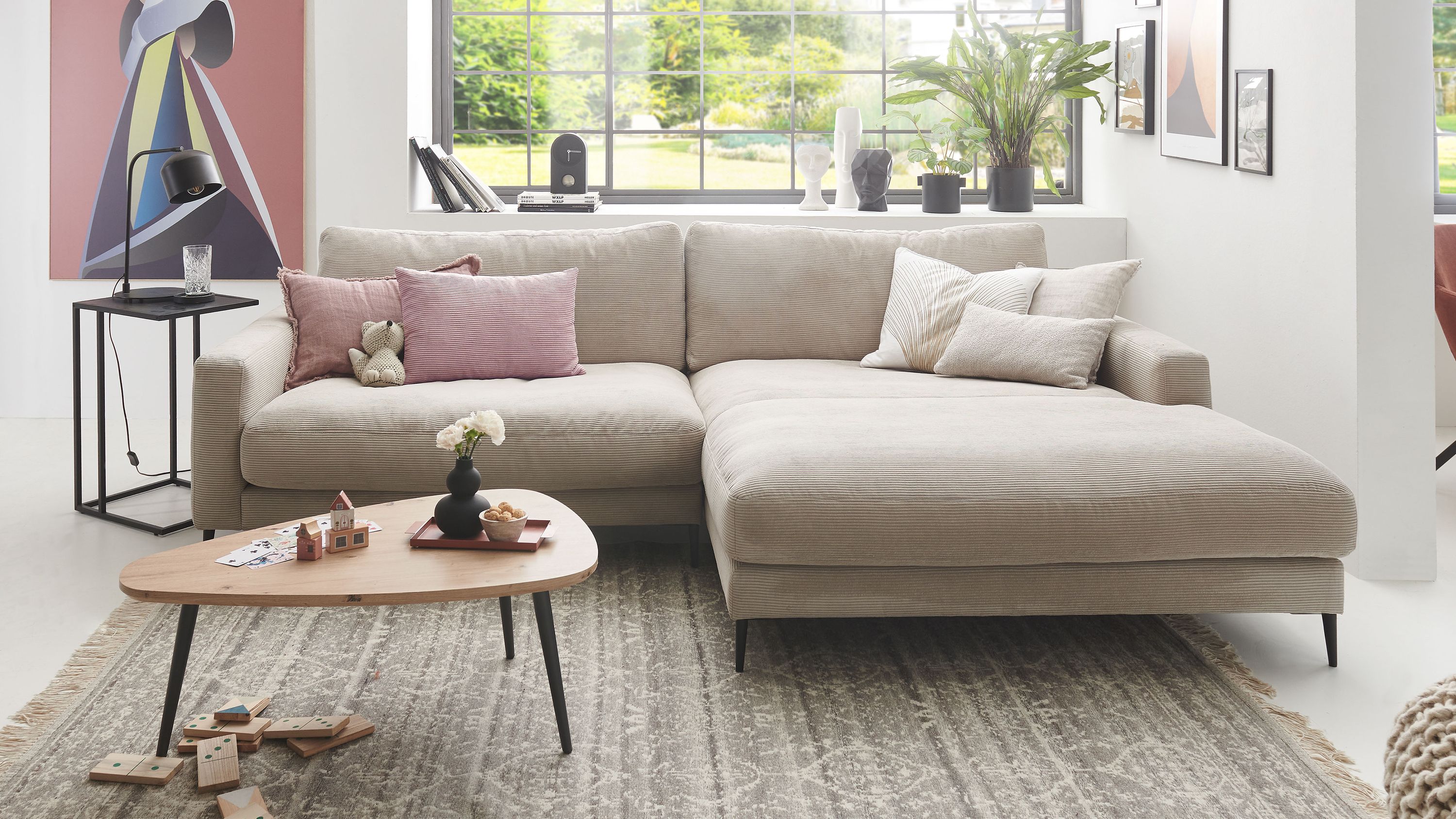 Ecksofa in sandfarbener Cordoptik mit schwarzen Metallfüßen und mehreren Kissen in hellem Wohnzimmer