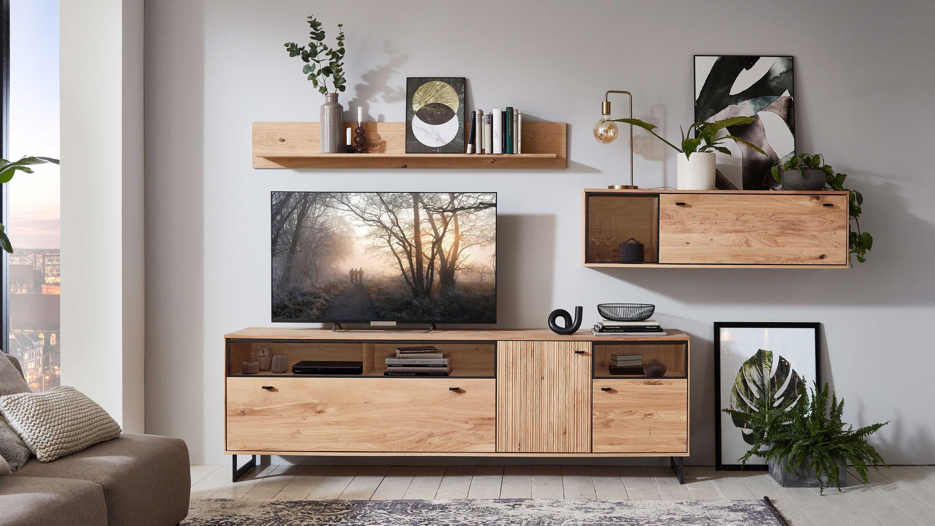 Dreiteilige Wohnwand aus hellem Holz mit Hängeschrank Dreiteilige Wohnwand aus hellem Holz mit offenen Fächern Schubladen und Hängeschrank an grauer Wand