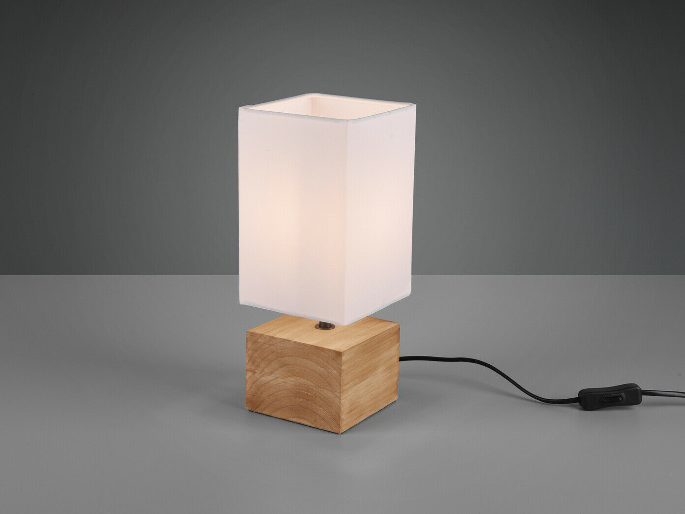 Tischlampe mit Holzfuß und weißem rechteckigem Schirm auf grauer Fläche, Stromkabel sichtbar