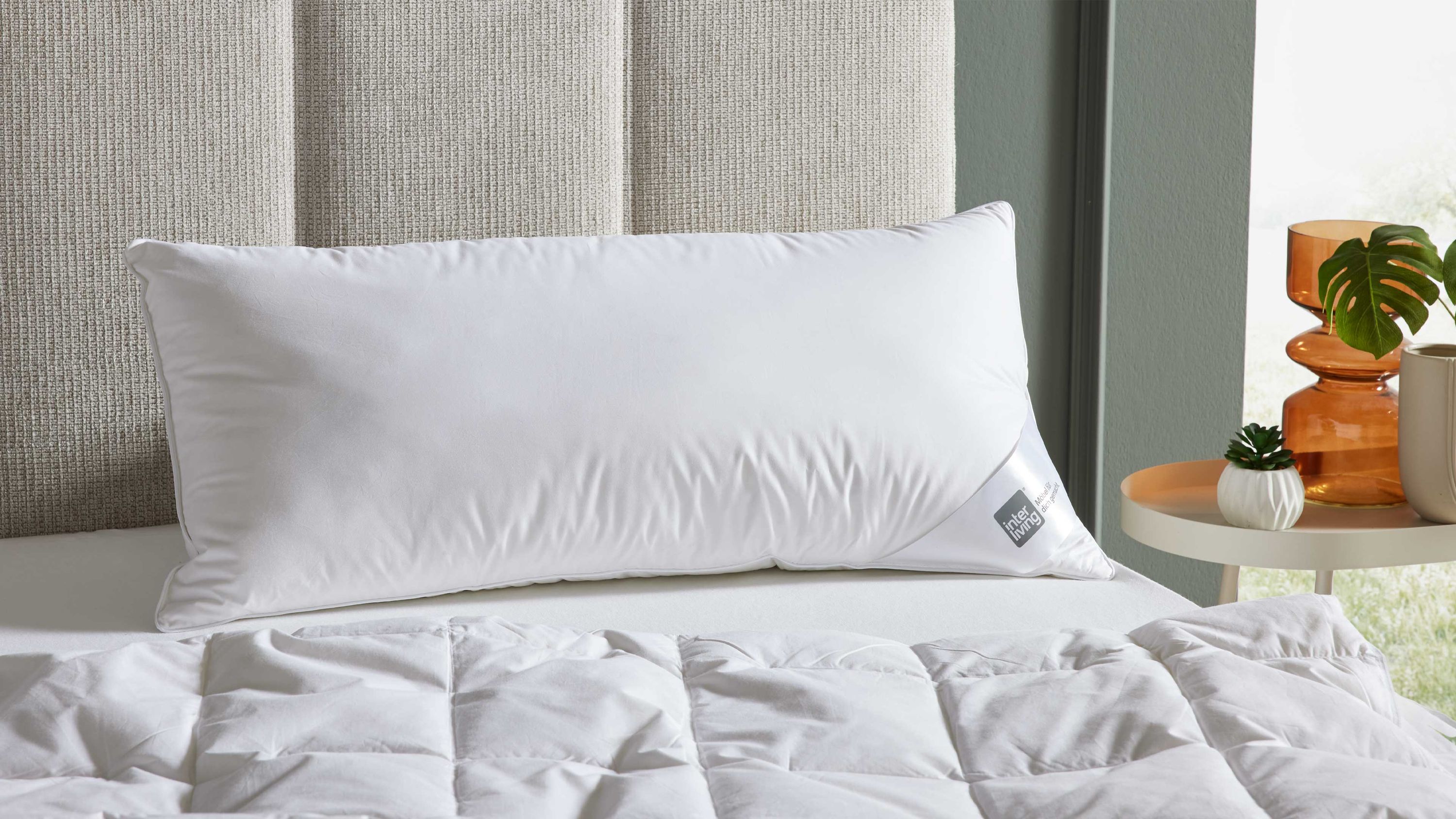 Langes weißes Kopfkissen mit drei Kammern auf einem Bett mit weißer Bettdecke und beigem Kopfteil