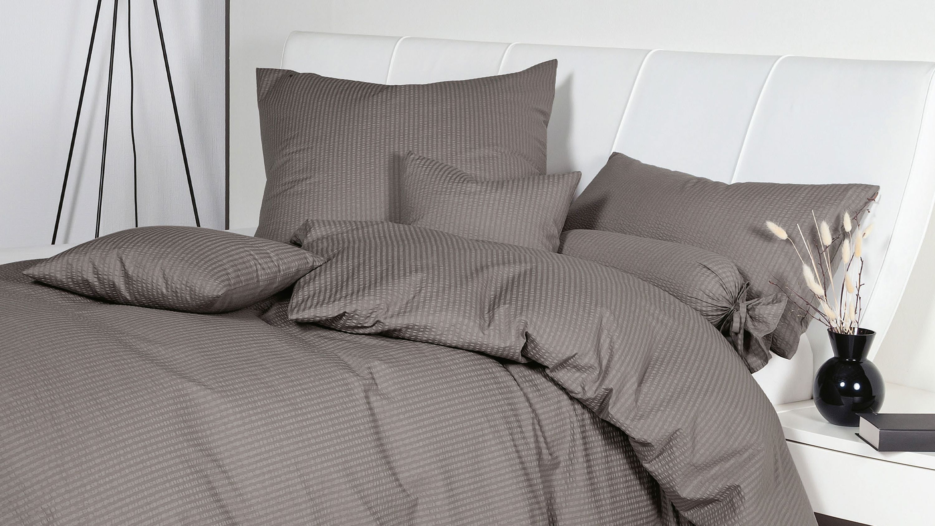 Bett mit brauner Bettwäsche und mehreren Kissen vor weißem gepolstertem Kopfteil