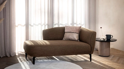 Recamiere mit Beistelltisch im modernen Wohnambiente. Moderne Recamiere in Braun mit Zierkissen steht vor bodentiefem Vorhang neben rundem Beistelltisch mit Tasse.