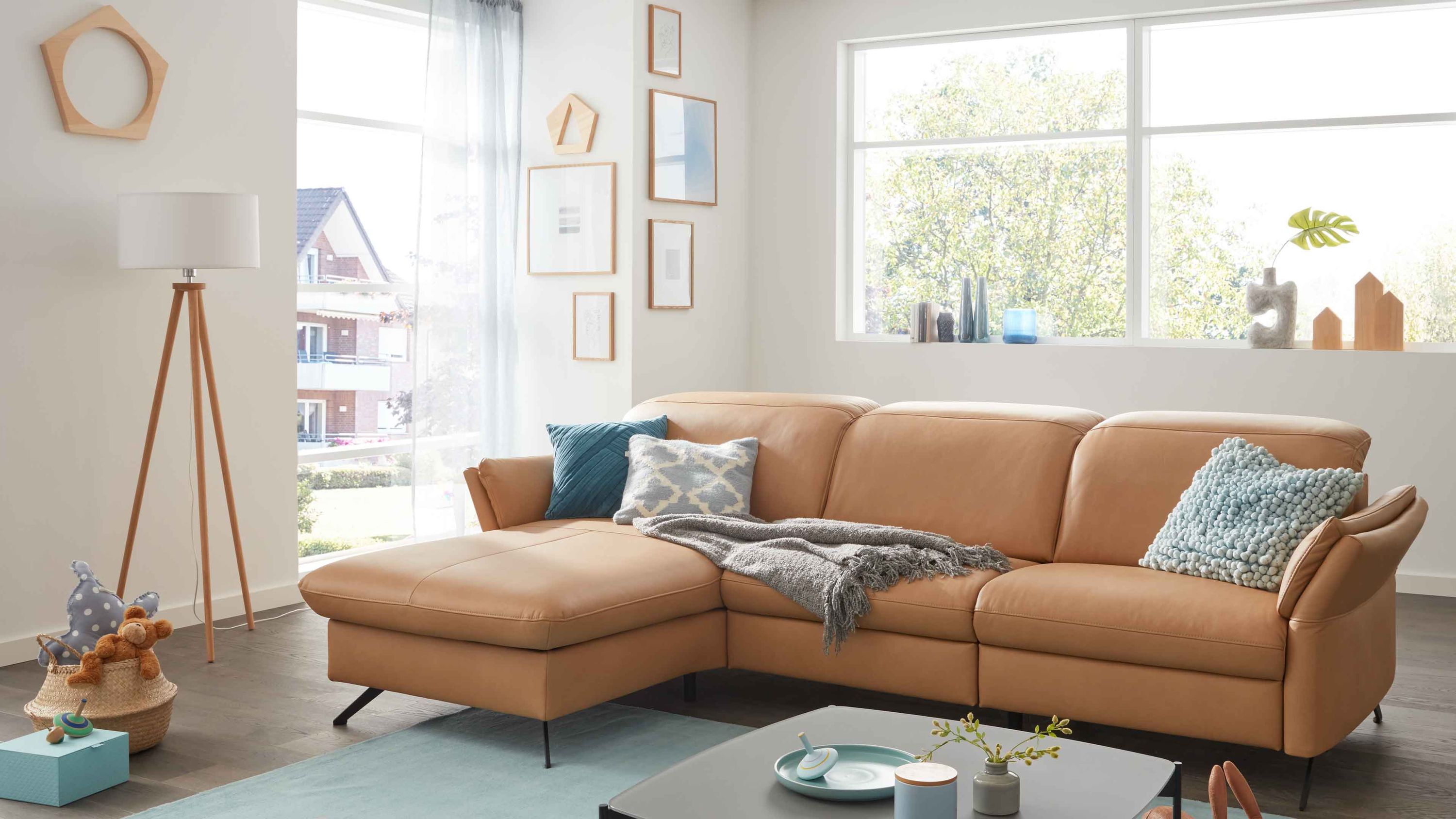 Ecksofa mit honigfarbenem Lederbezug und schwarzen Metallfüßen in modernem Wohnzimmer mit Fenster