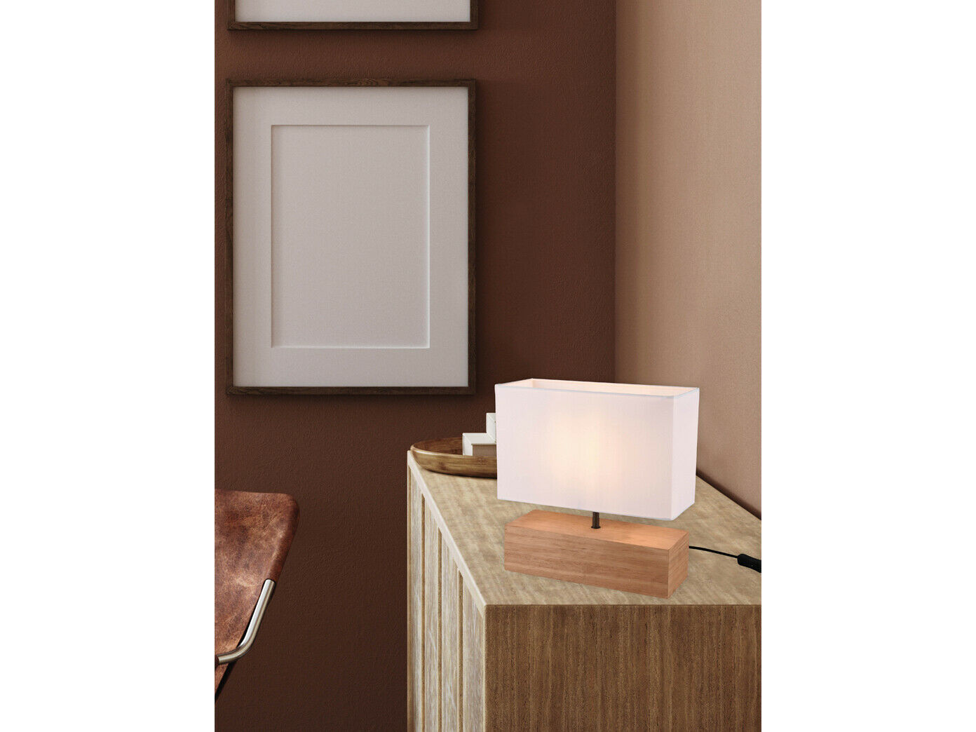 Tischlampe mit Holzfuß textilschirm beleuchtet Tischleuchte mit weißem Textilschirm und braunem Holzsockel auf hellem Sideboard vor brauner Wand mit Wanddekor Licht an